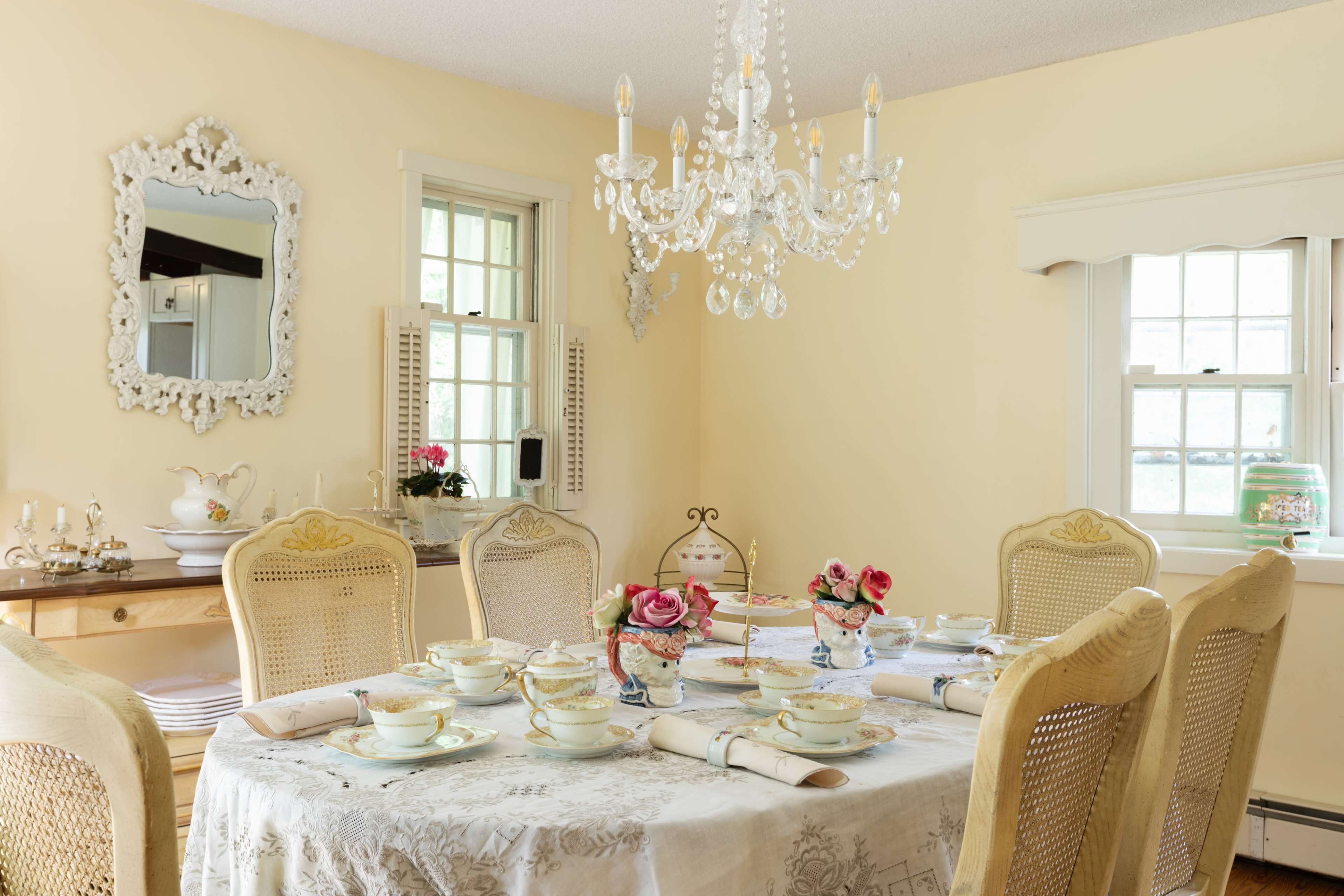 The dining room features a table set with fine china, embellished with floral designs, and surrounded by elegant chairs beneath a crystal chandelier.