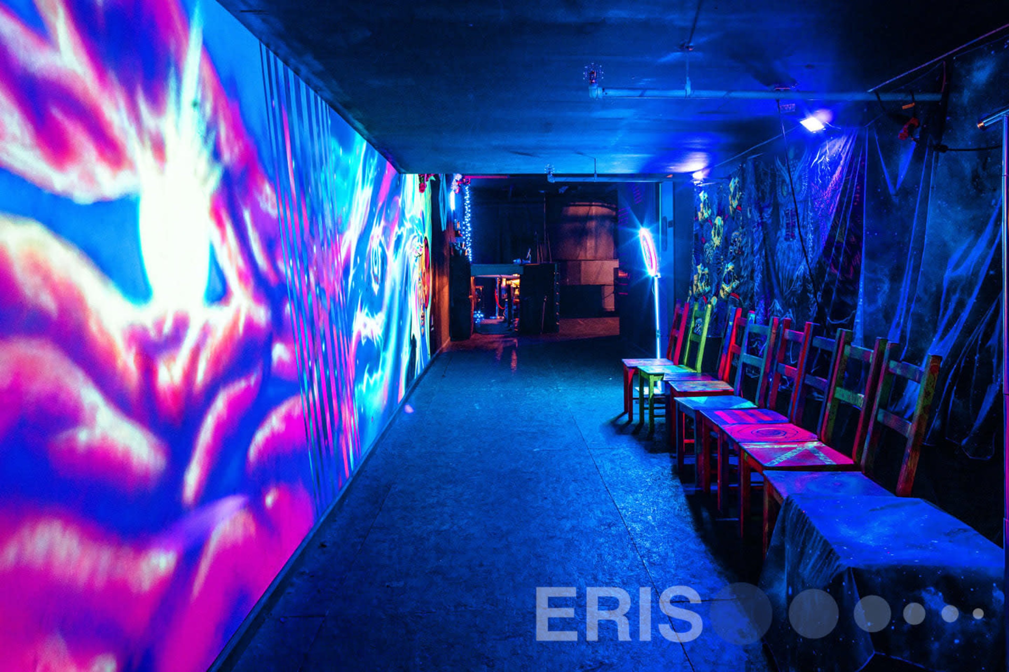 A dimly lit corridor with vibrant, colorful projections on the walls and several chairs lined up on one side.