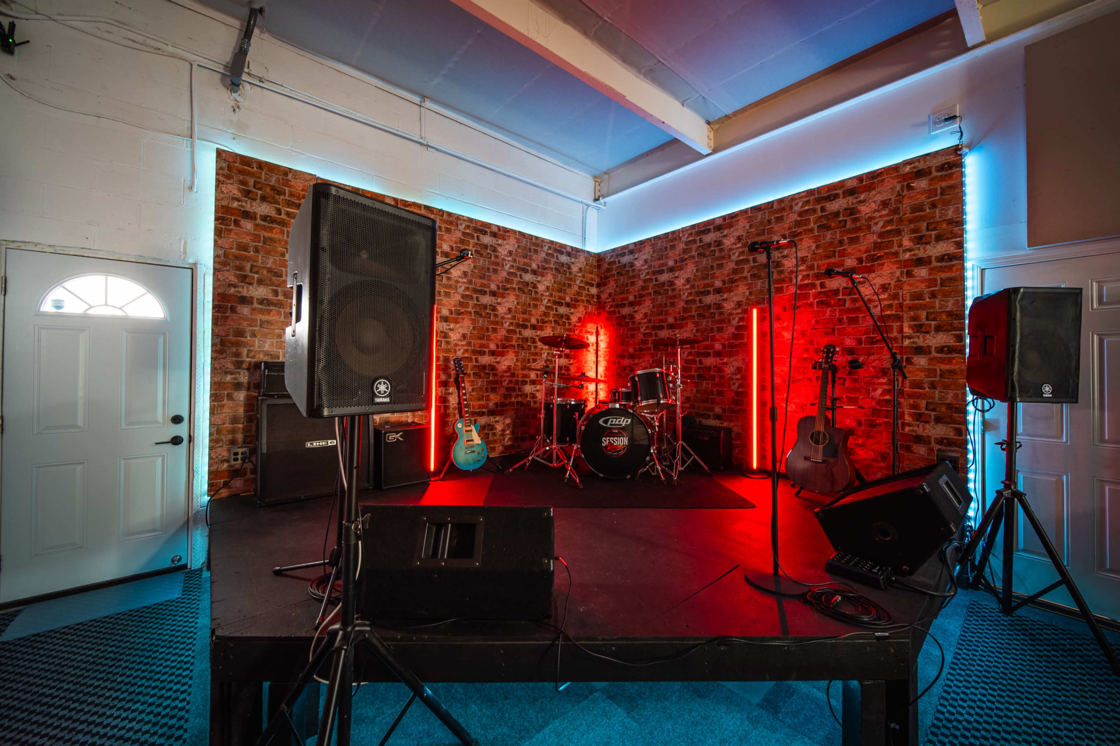 A performance stage is set up with musical instruments, amplifiers, and a brick wall backdrop illuminated by colorful lights.