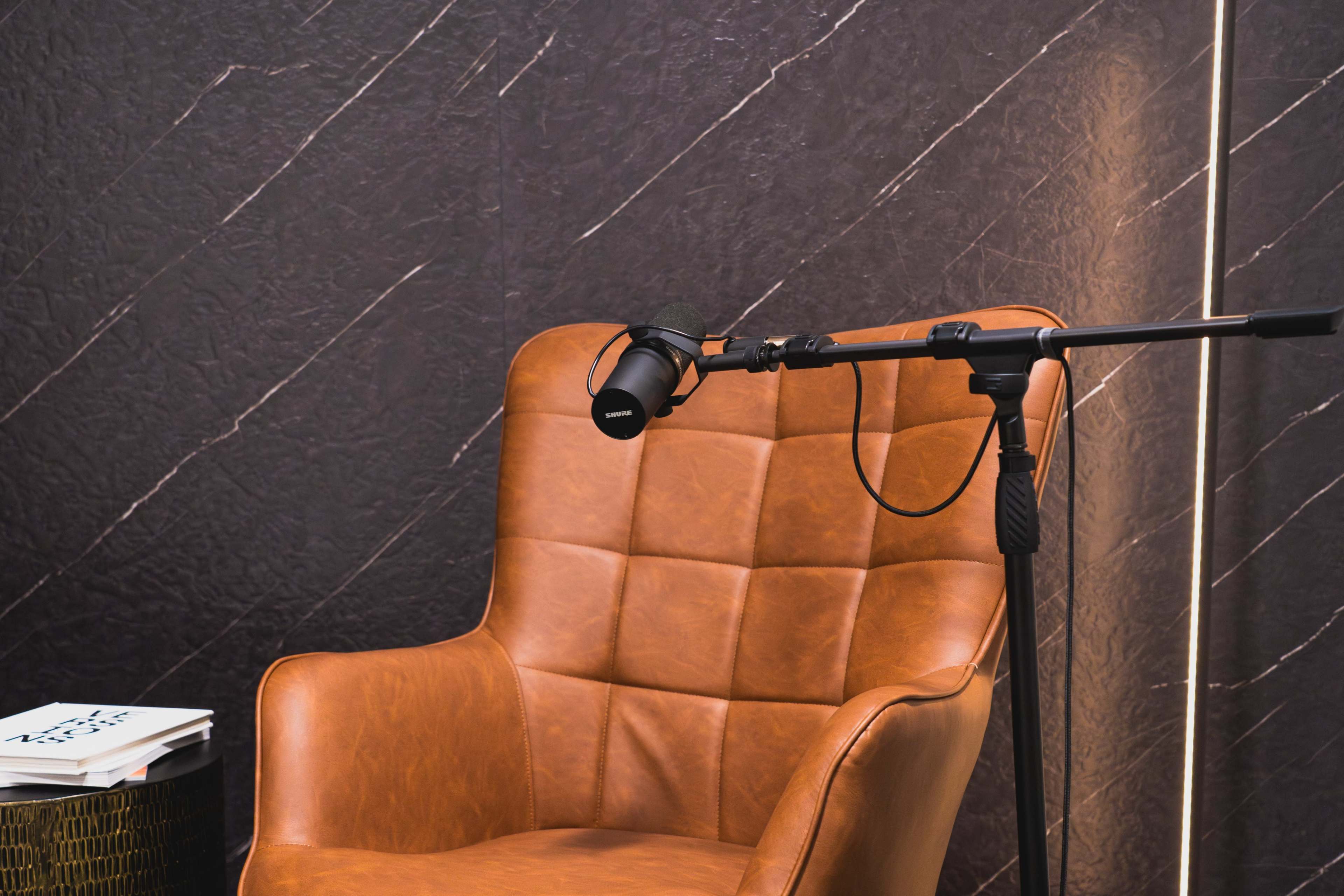 A brown leather chair is positioned next to a microphone on a stand, against a textured wall.