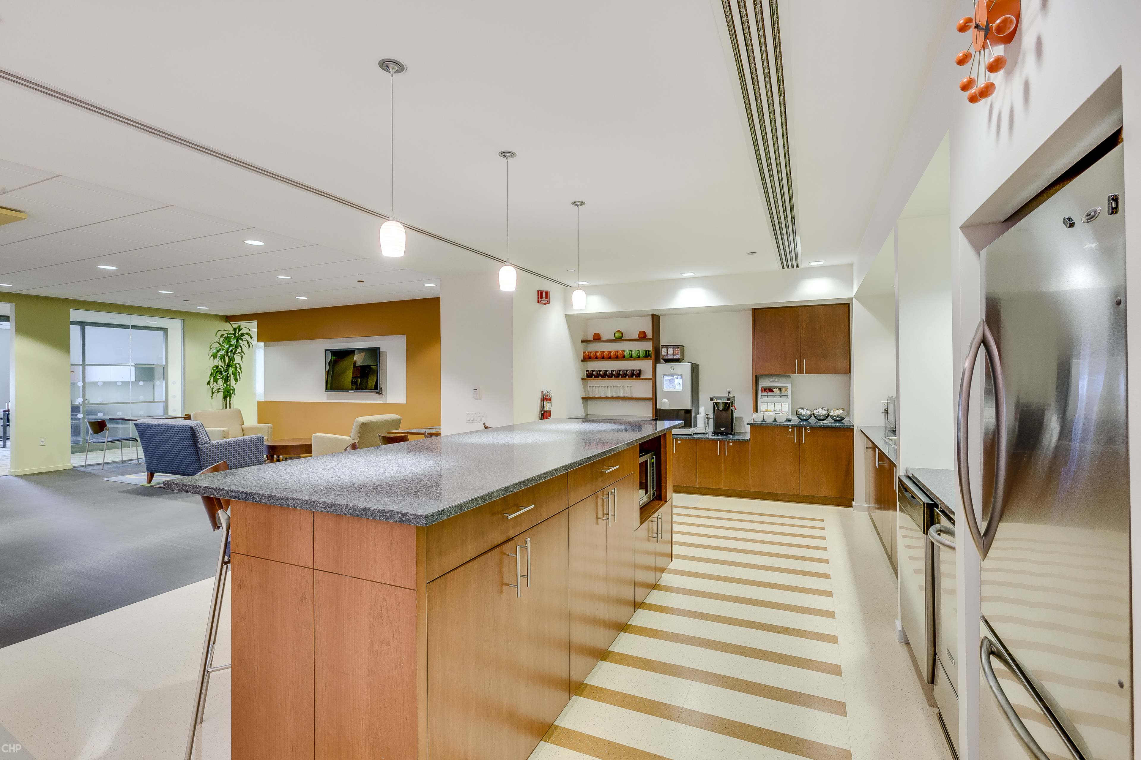 The image shows a modern kitchen with wooden cabinets, a countertop, and appliances, situated in a spacious, well-lit room.
