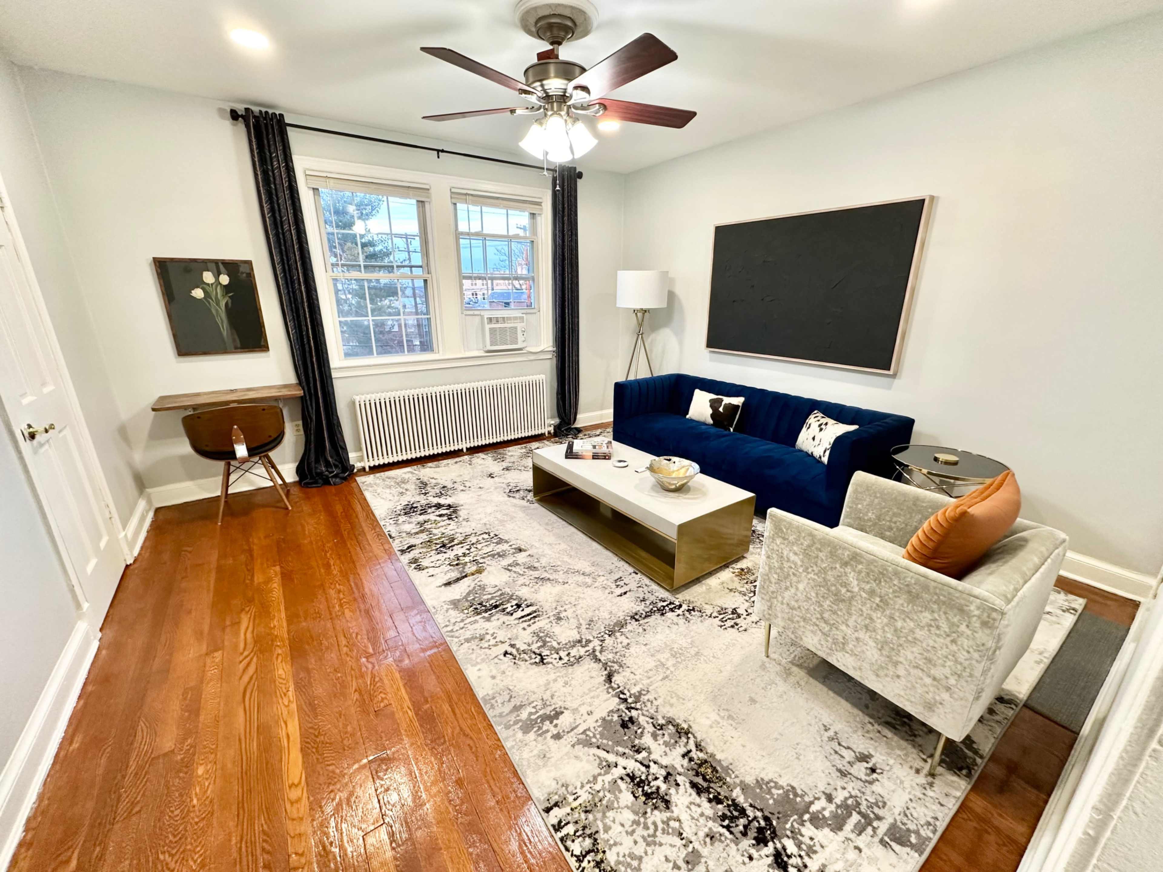The living room features a blue sofa, a light gray armchair, a wooden table, a large area rug, and a chalkboard on the wall, with a window providing natural light.
