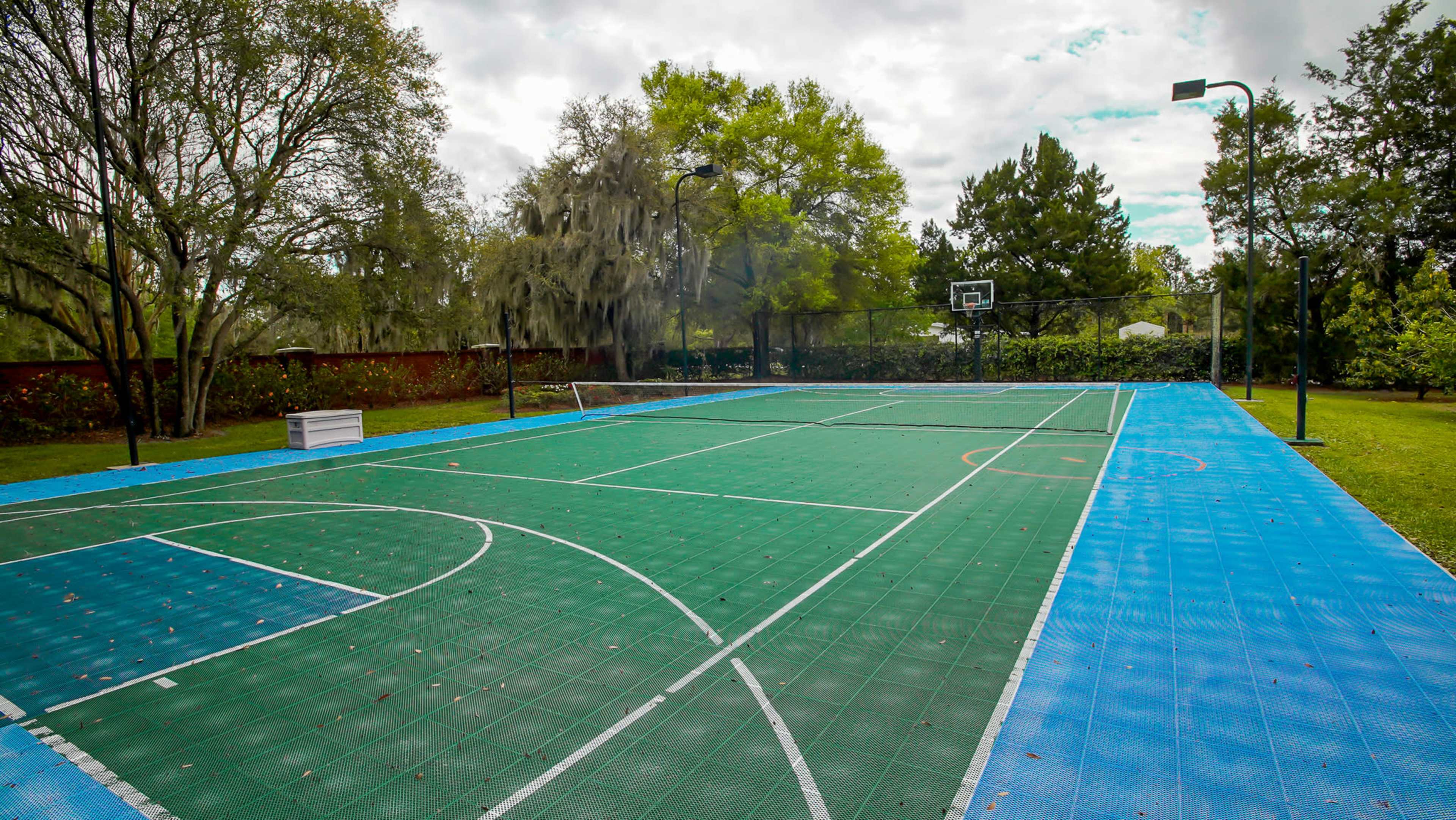 A multi-court sports facility with a green and blue surface, featuring basketball hoops and marked lines for basketball and possibly other games, set in a grassy outdoor area.