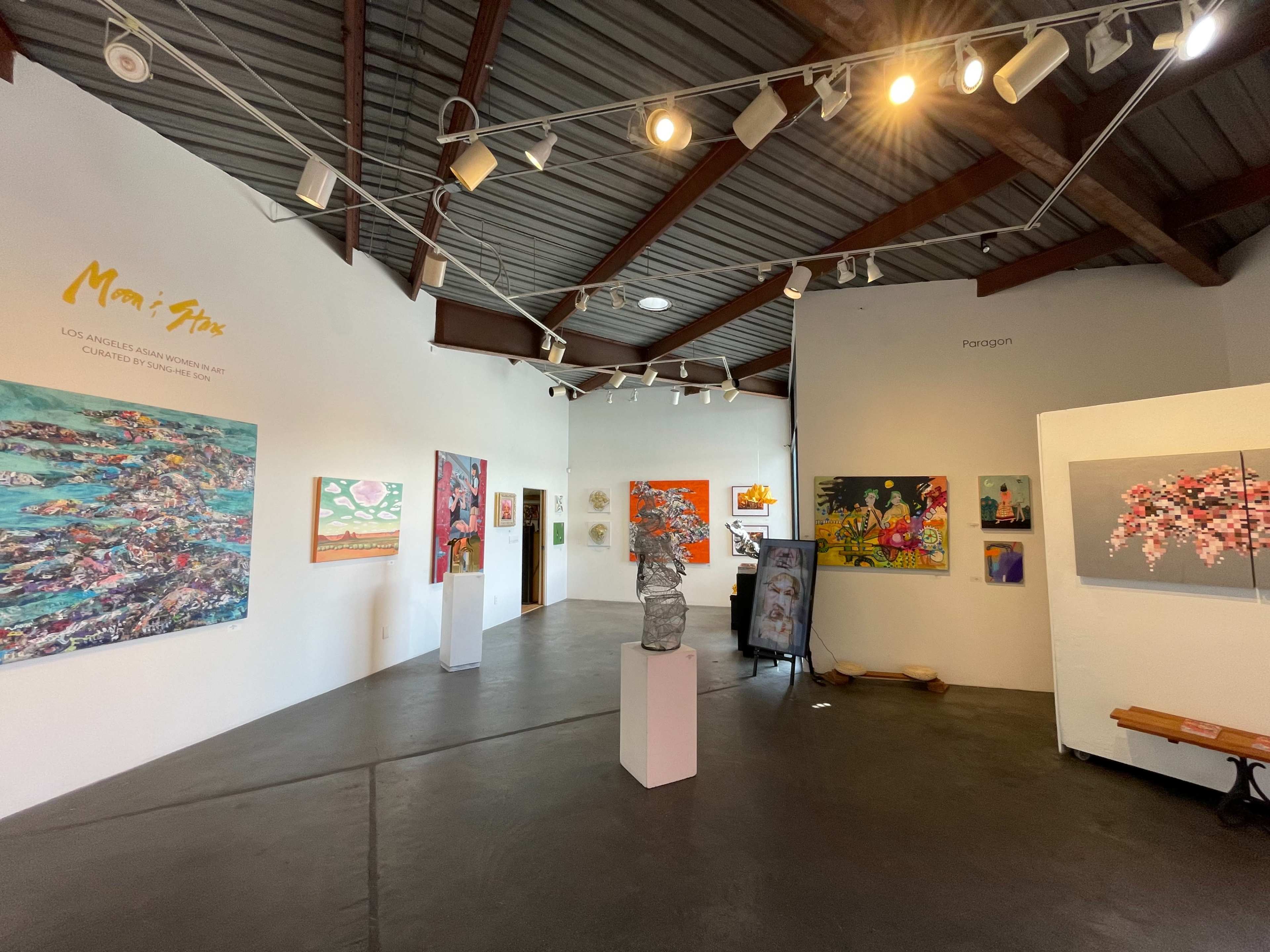 An indoor art gallery with various colorful artworks displayed on the walls and a sculpture in the center.