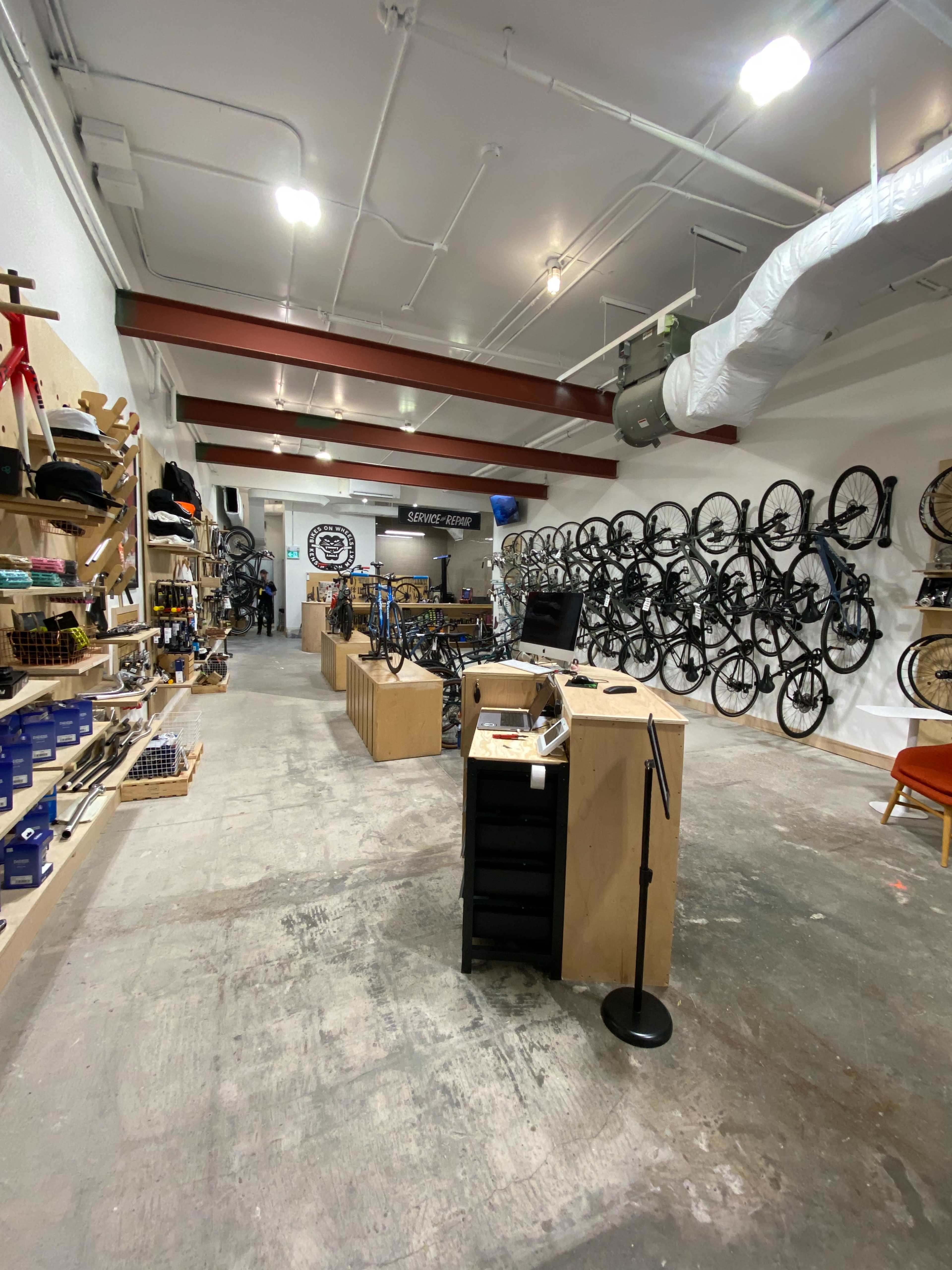 The image shows an indoor bike shop with walls lined with bicycles and wooden shelves displaying various cycling accessories.