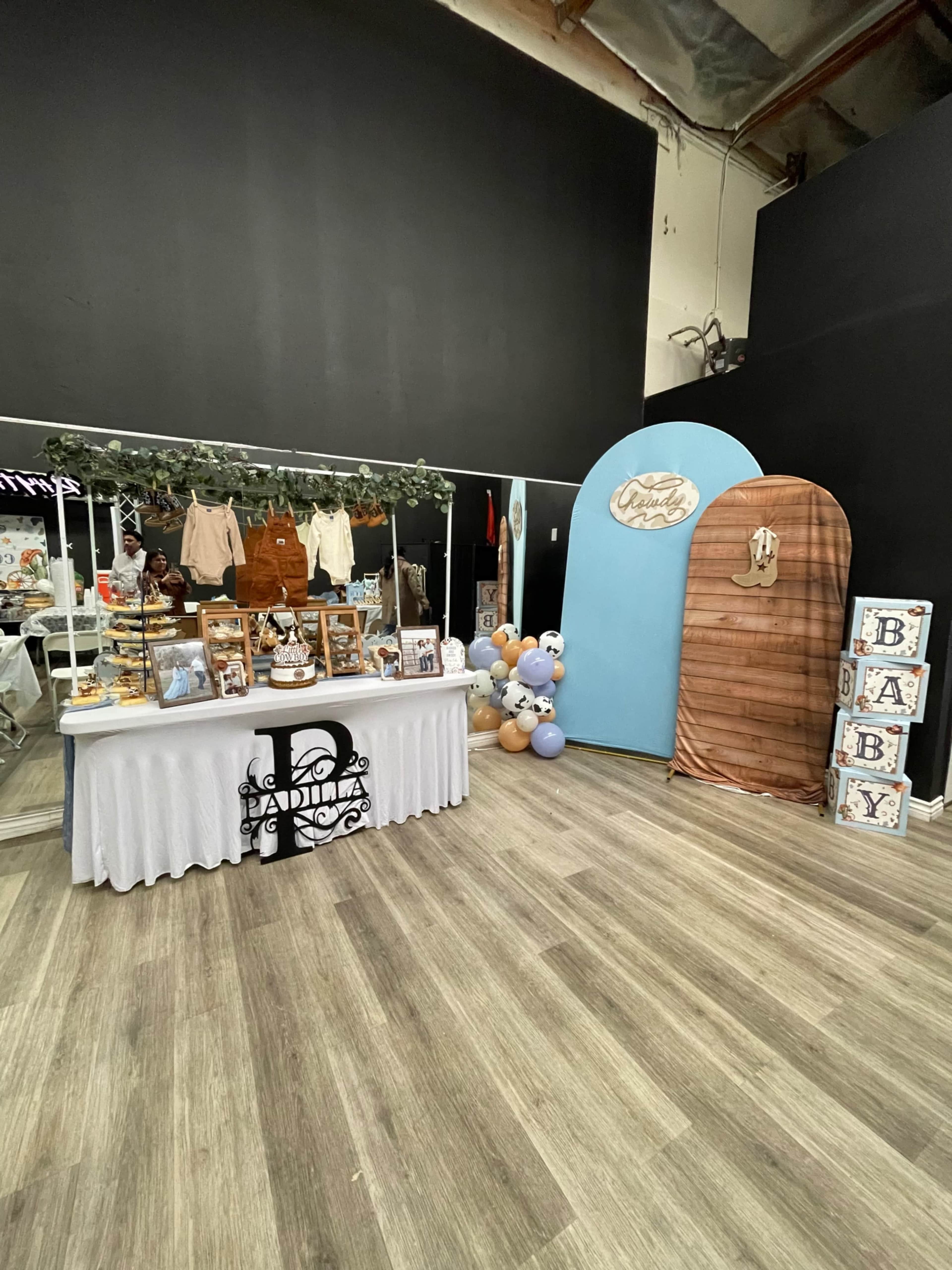 The image shows a decorated event space featuring a dessert table, a backdrop with an arch, and colorful balloons.