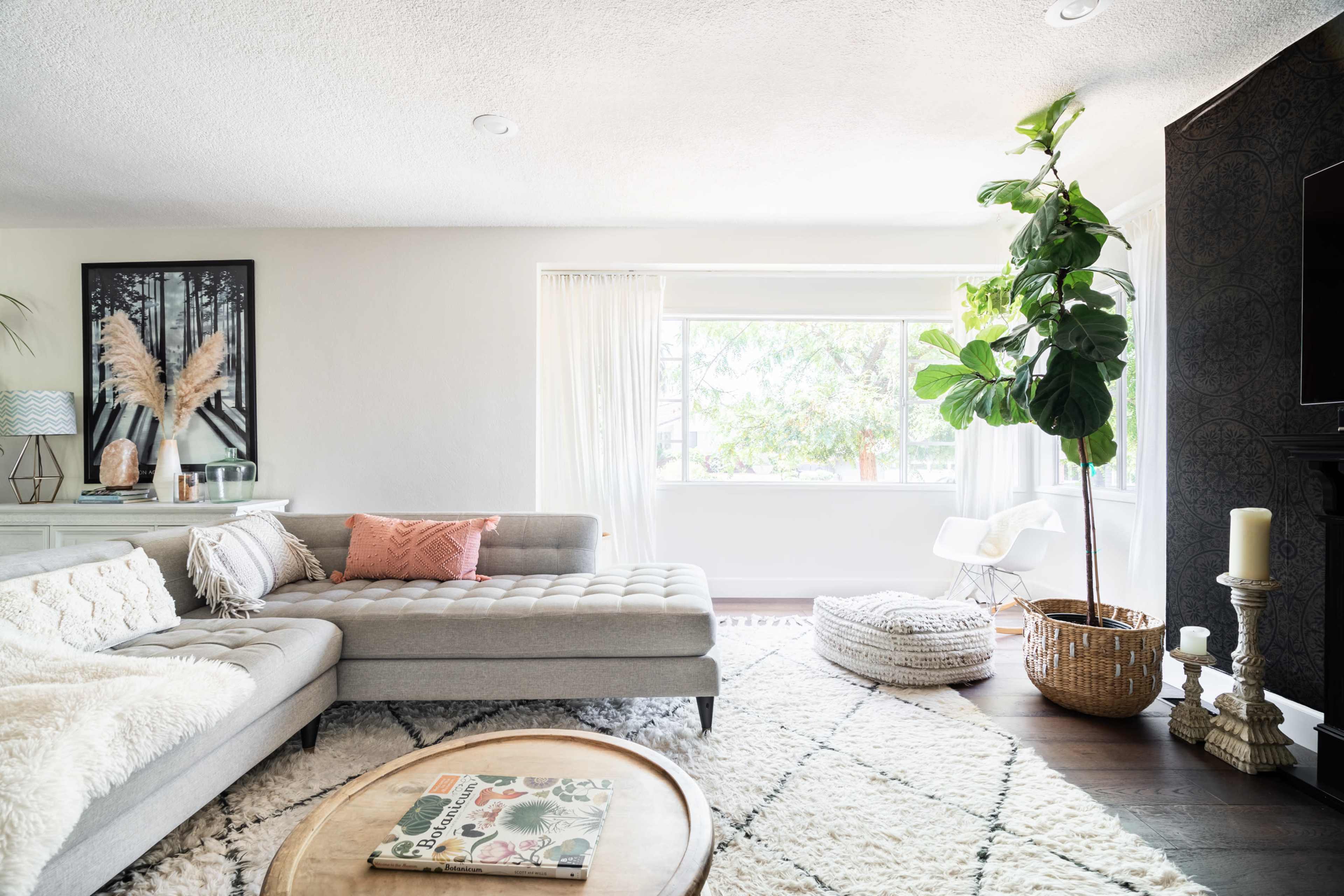 A modern living room featuring a gray sectional sofa, a large window with natural light, a potted plant, and a round coffee table with a decorative magazine.