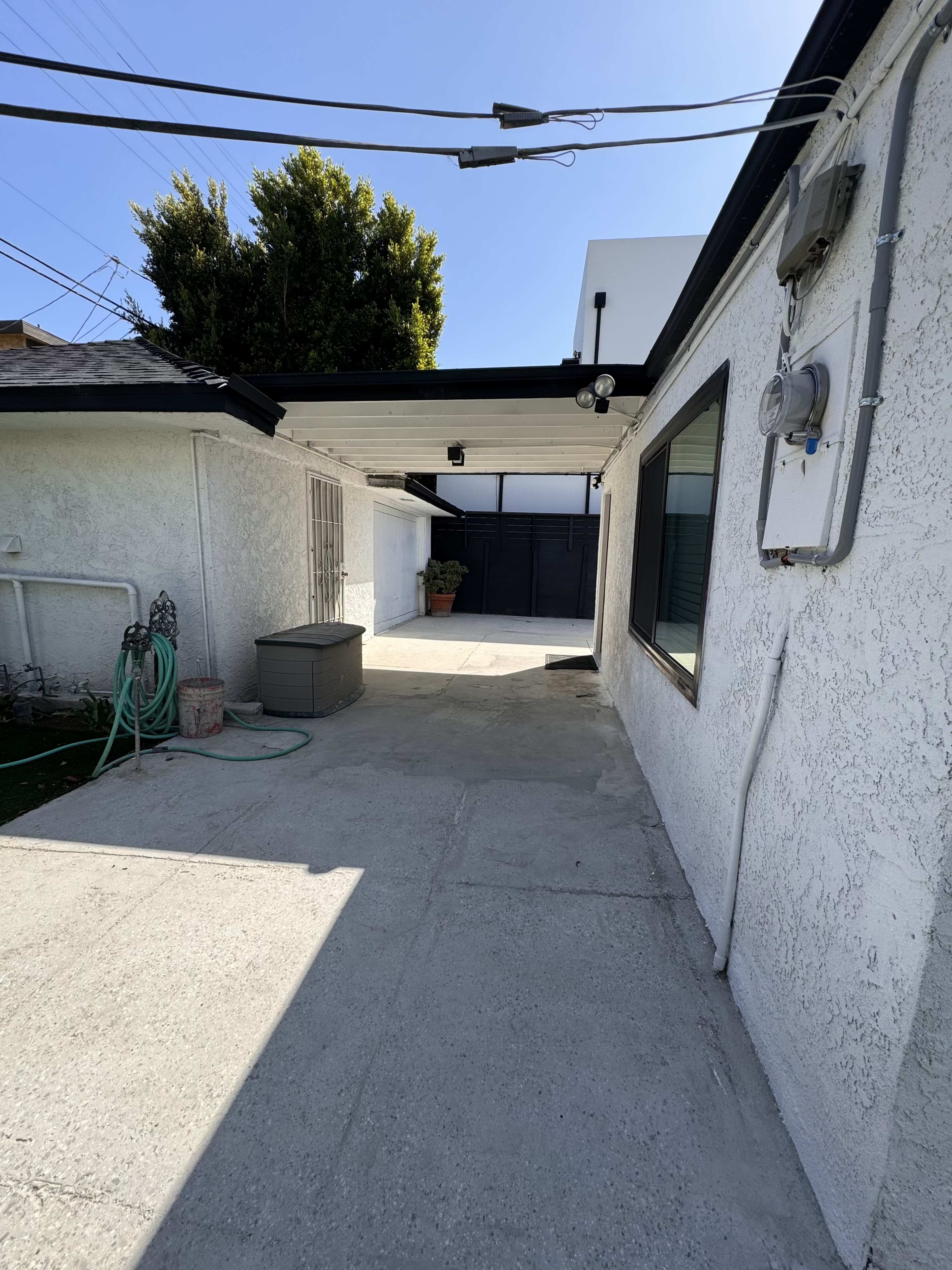The image shows a concrete pathway leading to a small courtyard with a wall and a power meter on the side of a house.