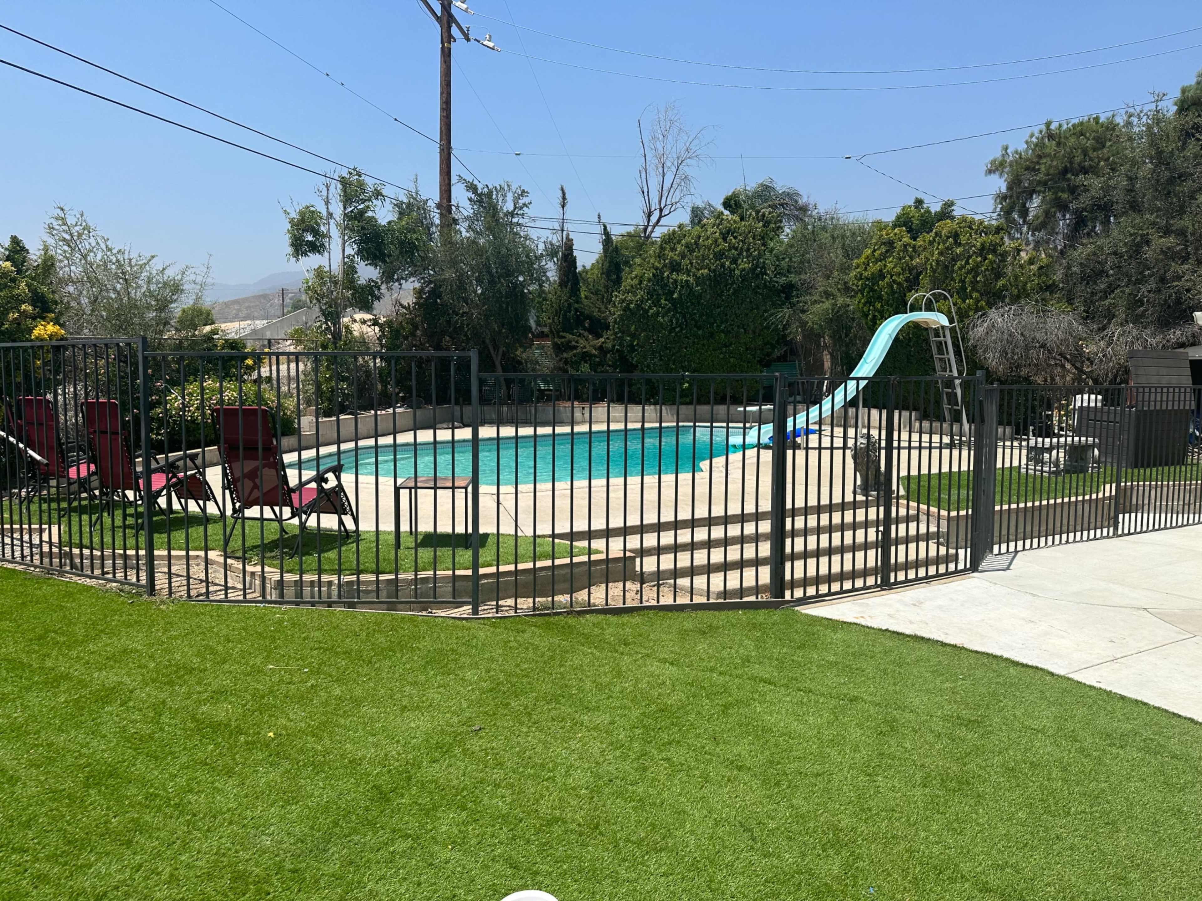 A fenced-in swimming pool surrounded by green grass and several lounge chairs.