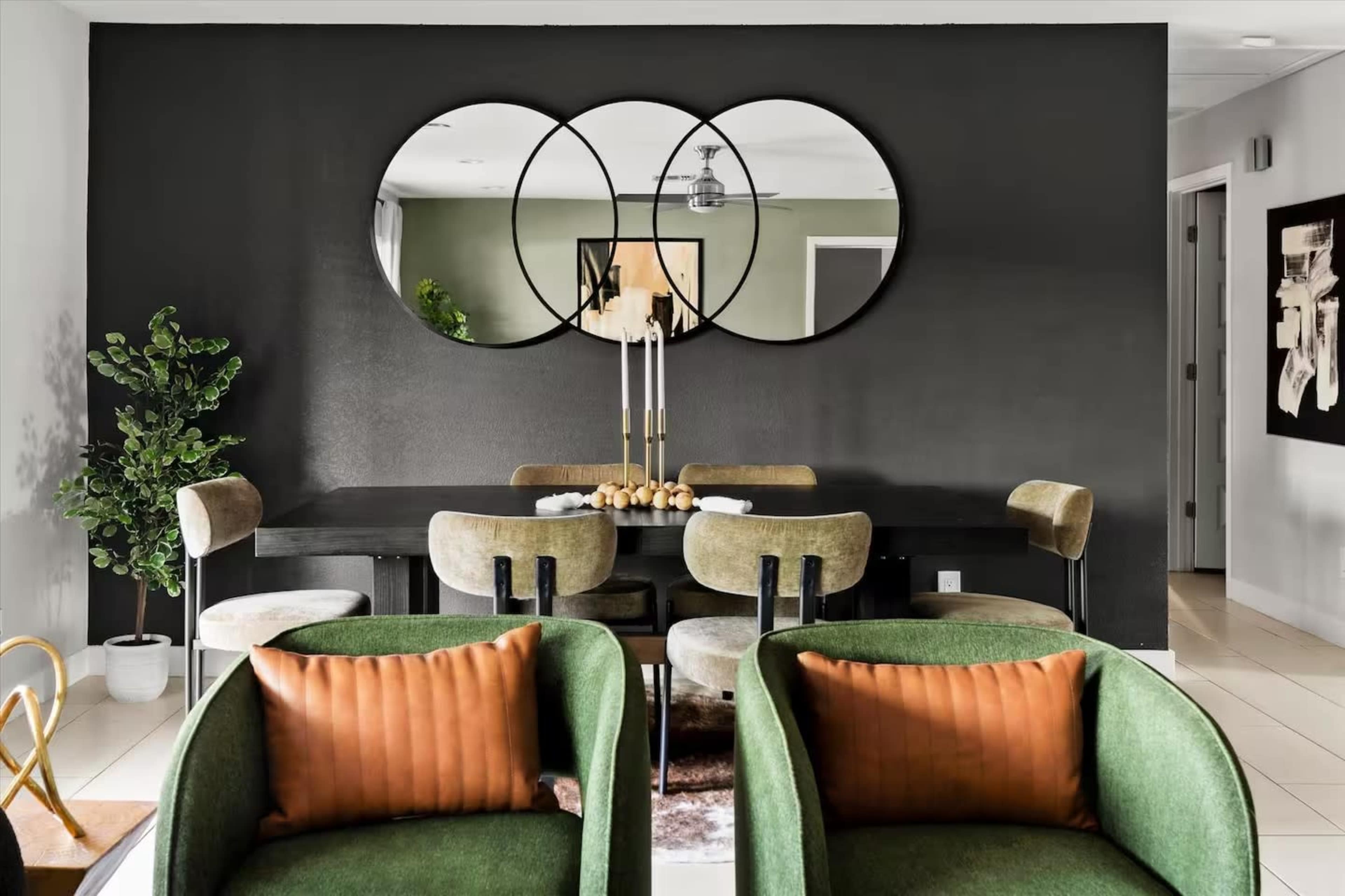 A modern dining area features a black wall with three circular mirrors, a rectangular table surrounded by chairs, and a small indoor plant in the corner.