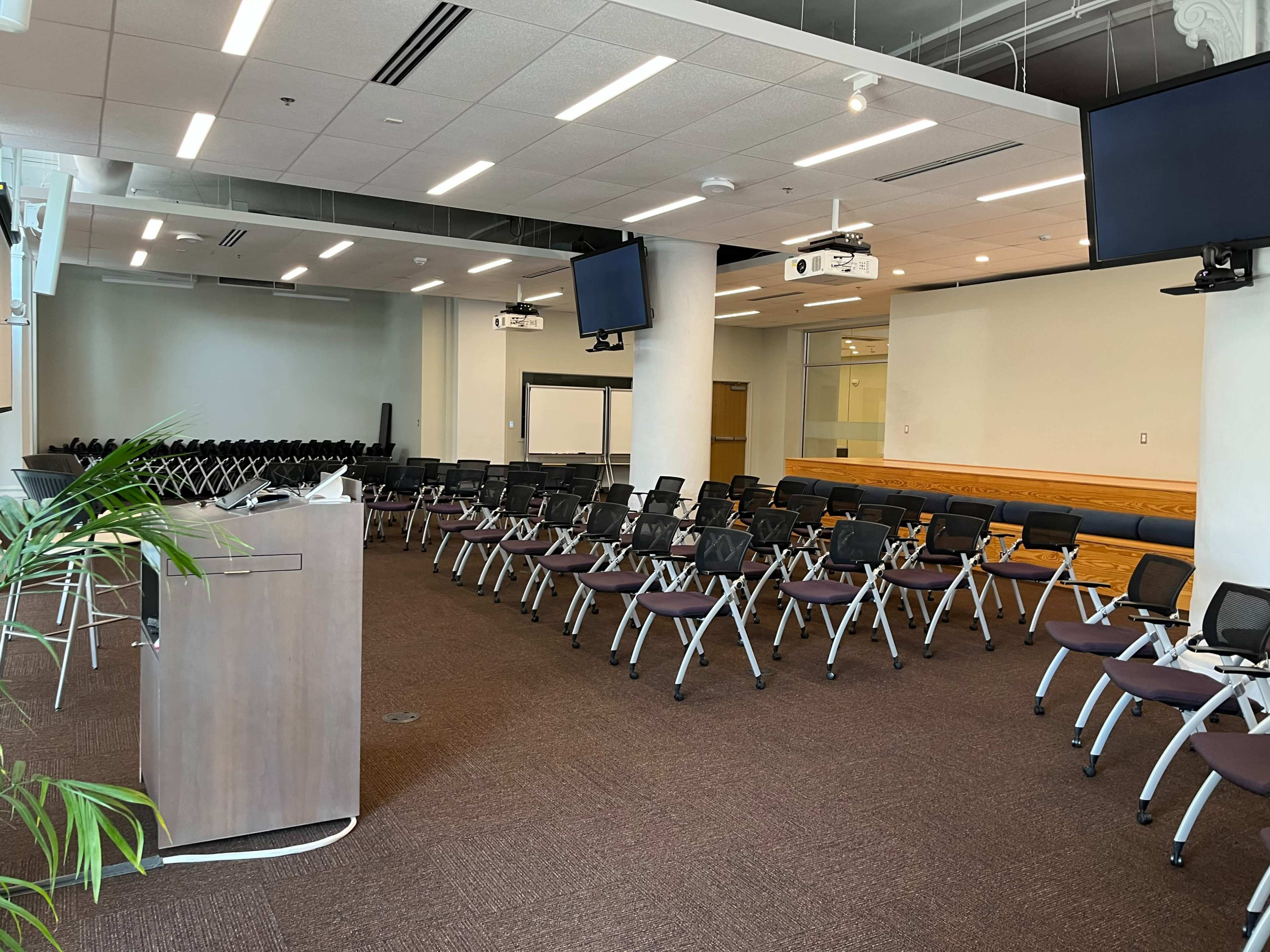 A conference room is set up with rows of chairs facing a podium and screens, ready for an event.