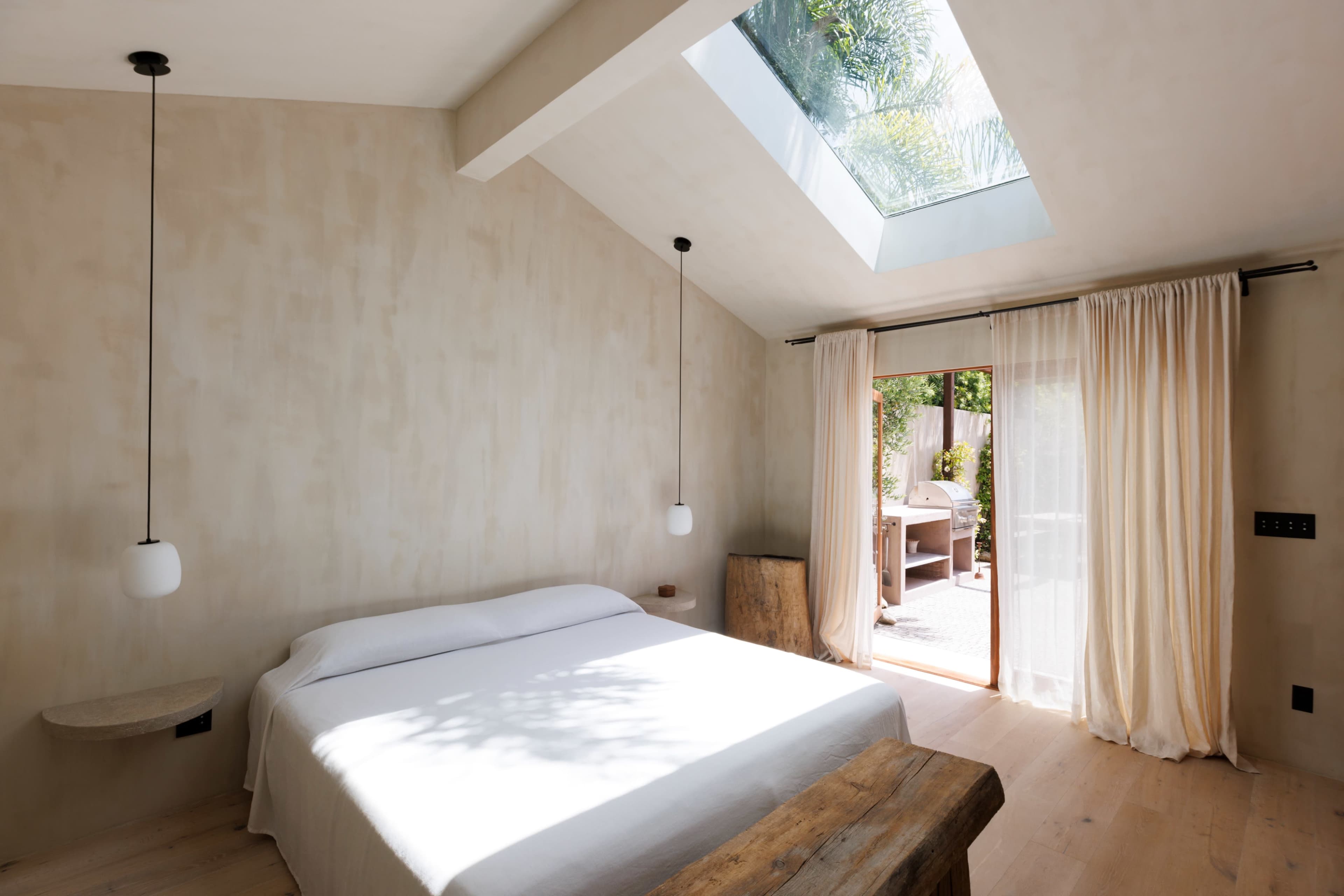 A minimalist bedroom featuring a bed, wooden accents, and a large window with a skylight providing natural light.