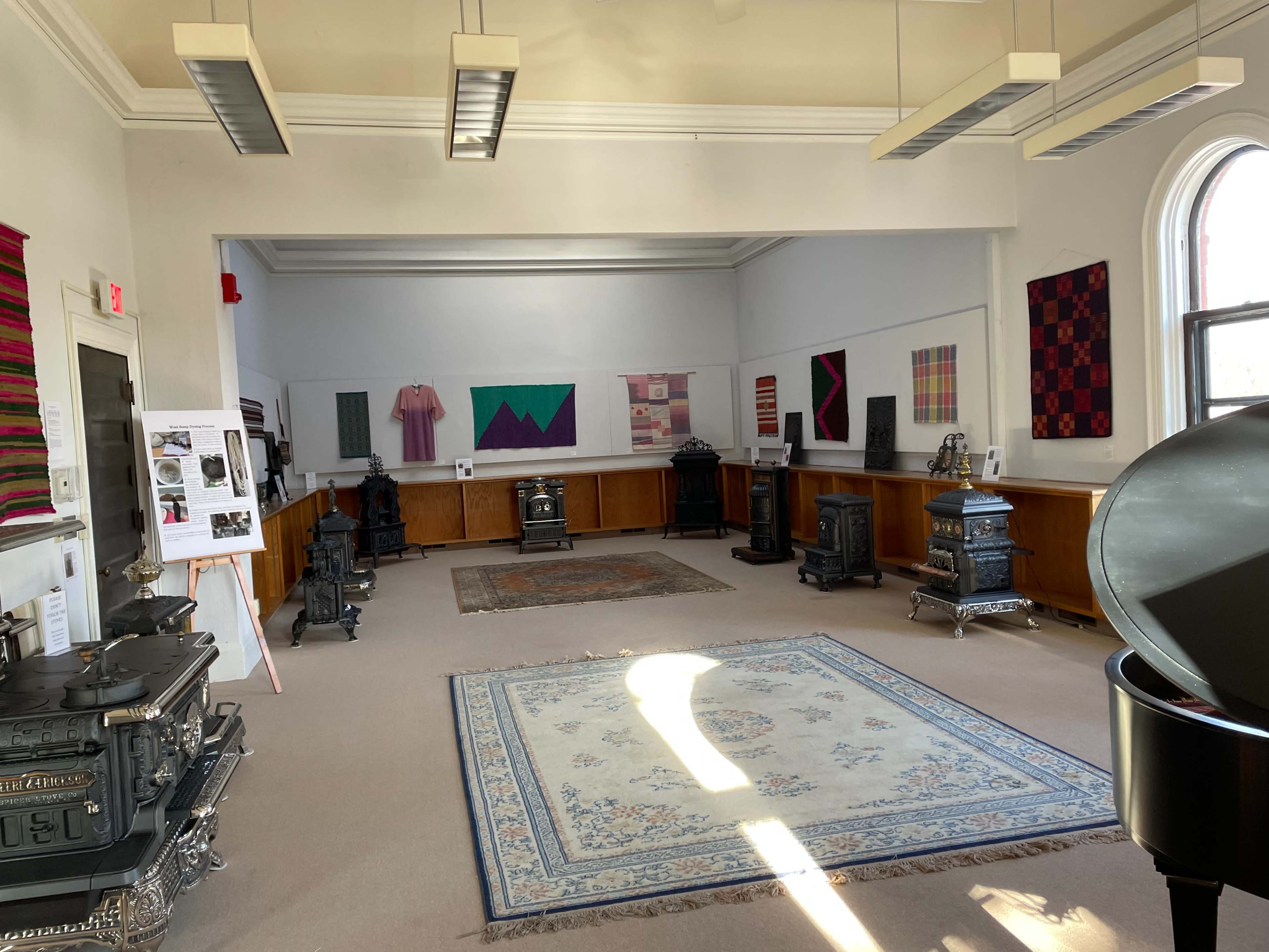 The spacious gallery features several ornate stoves, colorful wall hangings, and a large area rug on the floor.