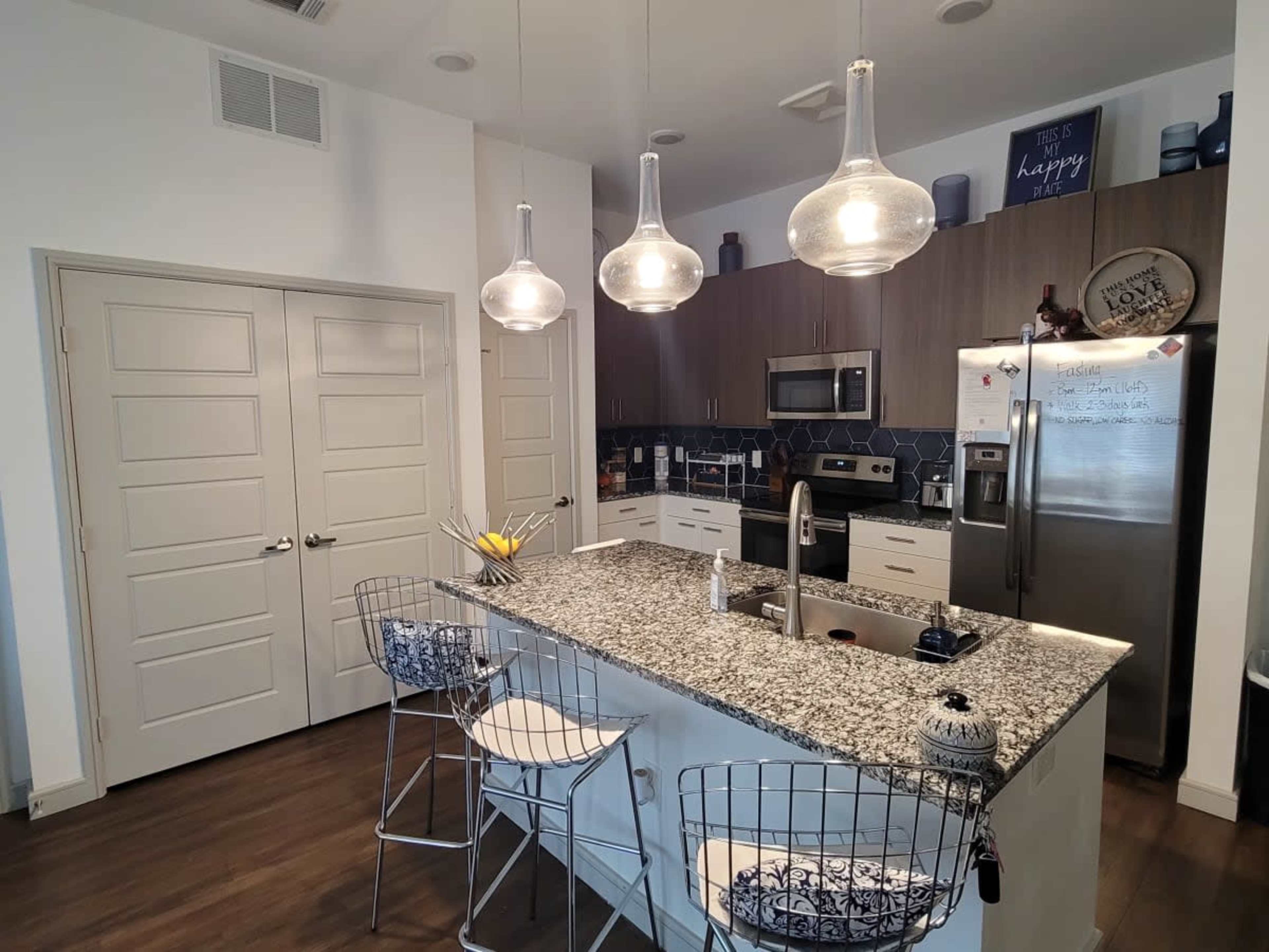 A modern kitchen featuring a central island with bar stools, stainless steel appliances, and pendant lighting.