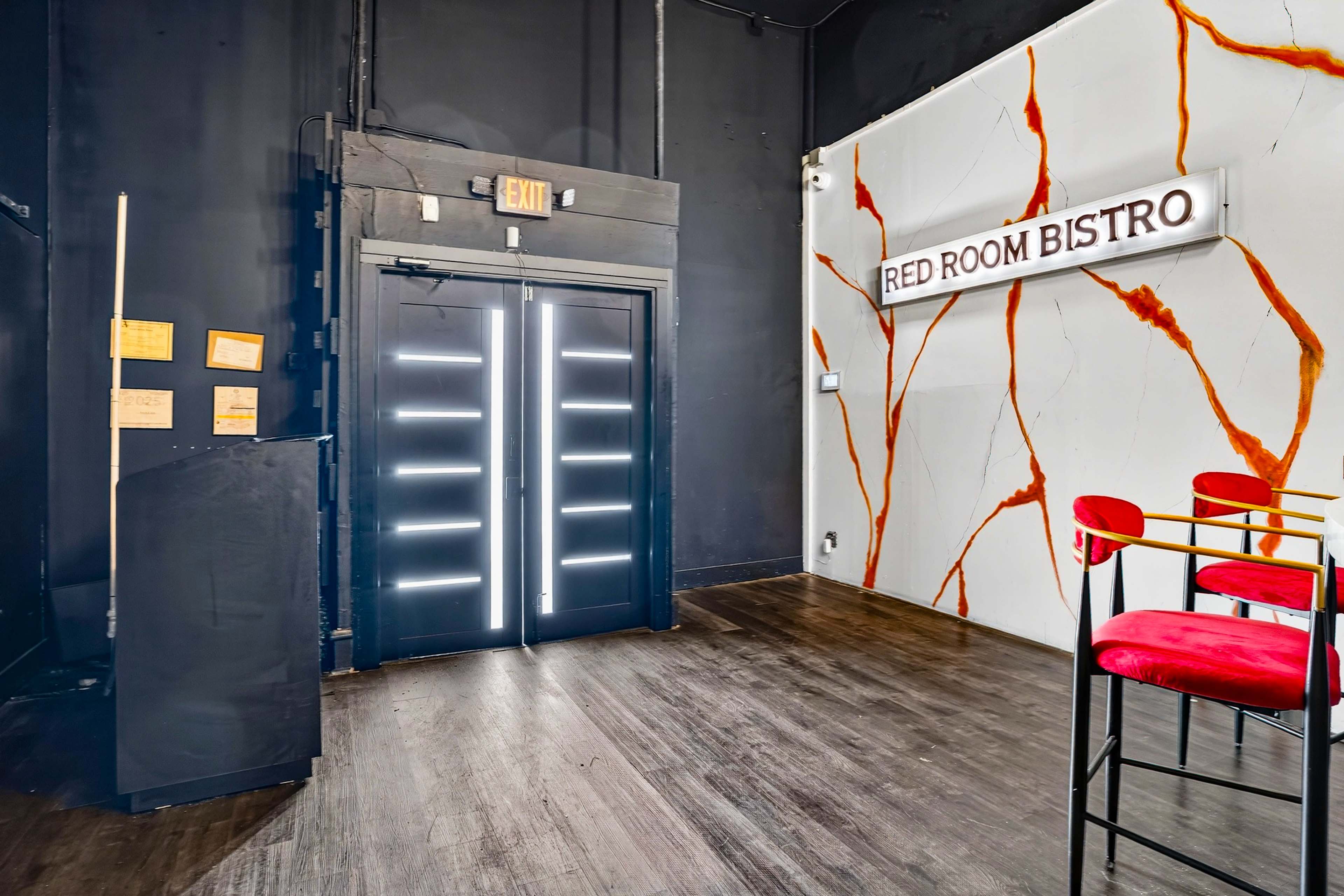 The image shows the interior of a restaurant called "Red Room Bistro," featuring a black wall, a striped entrance door with illuminated panels, and red bar stools against a marbled wall.