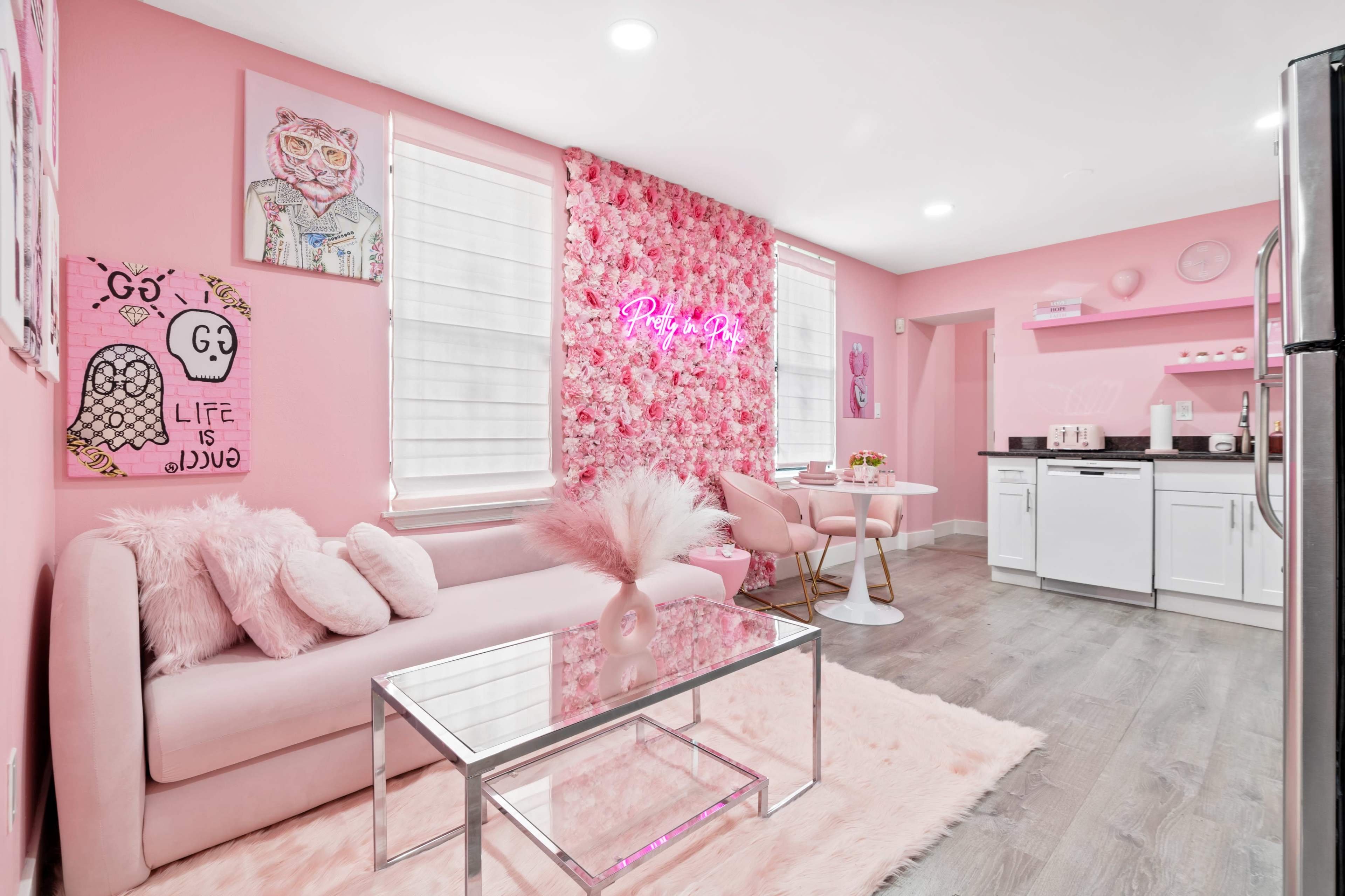 A bright pink-themed kitchen and living area featuring a floral accent wall, a glass coffee table, and modern furniture.