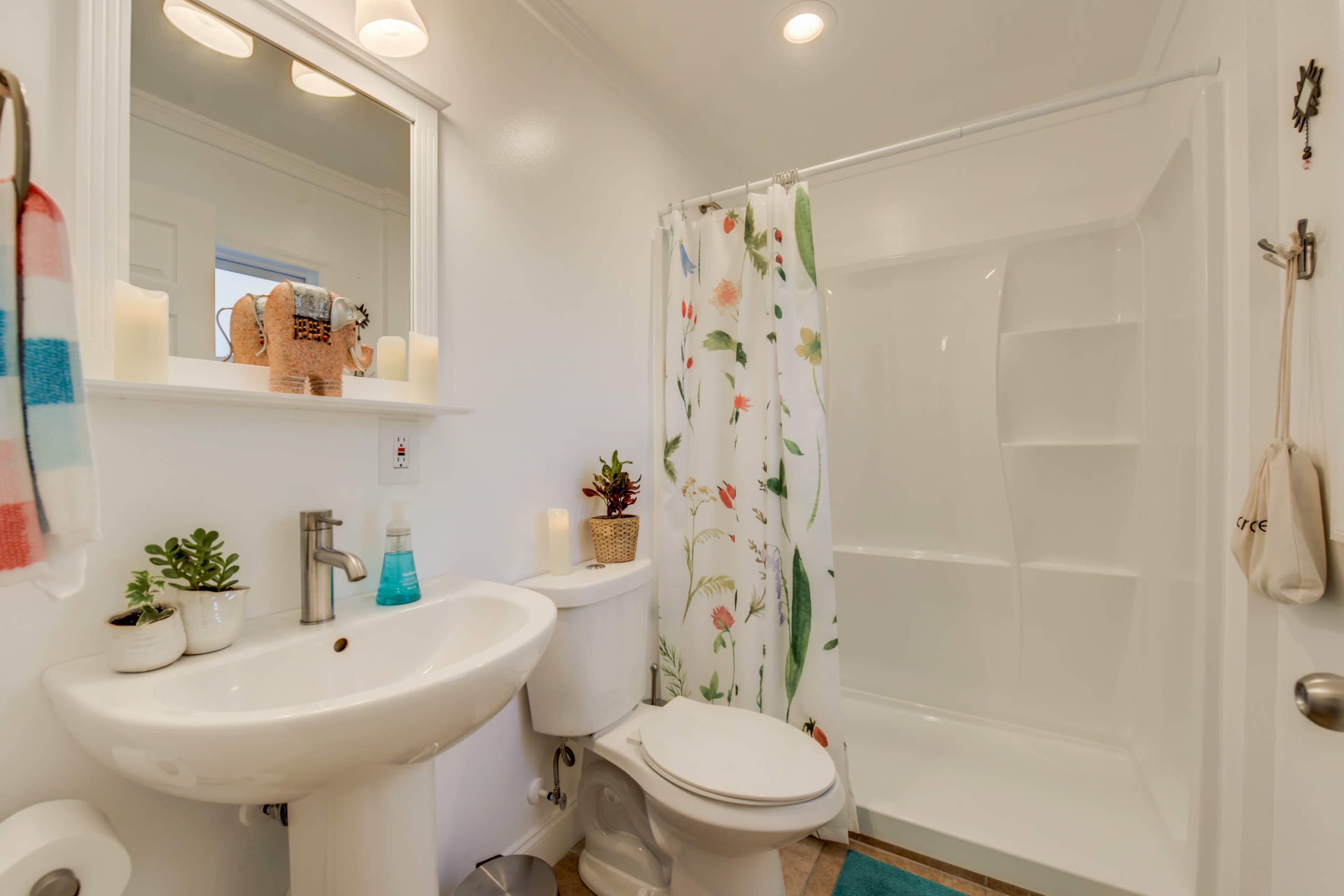A clean bathroom featuring a shower with a floral curtain, a sink with a mirror above it, and a toilet beside it.