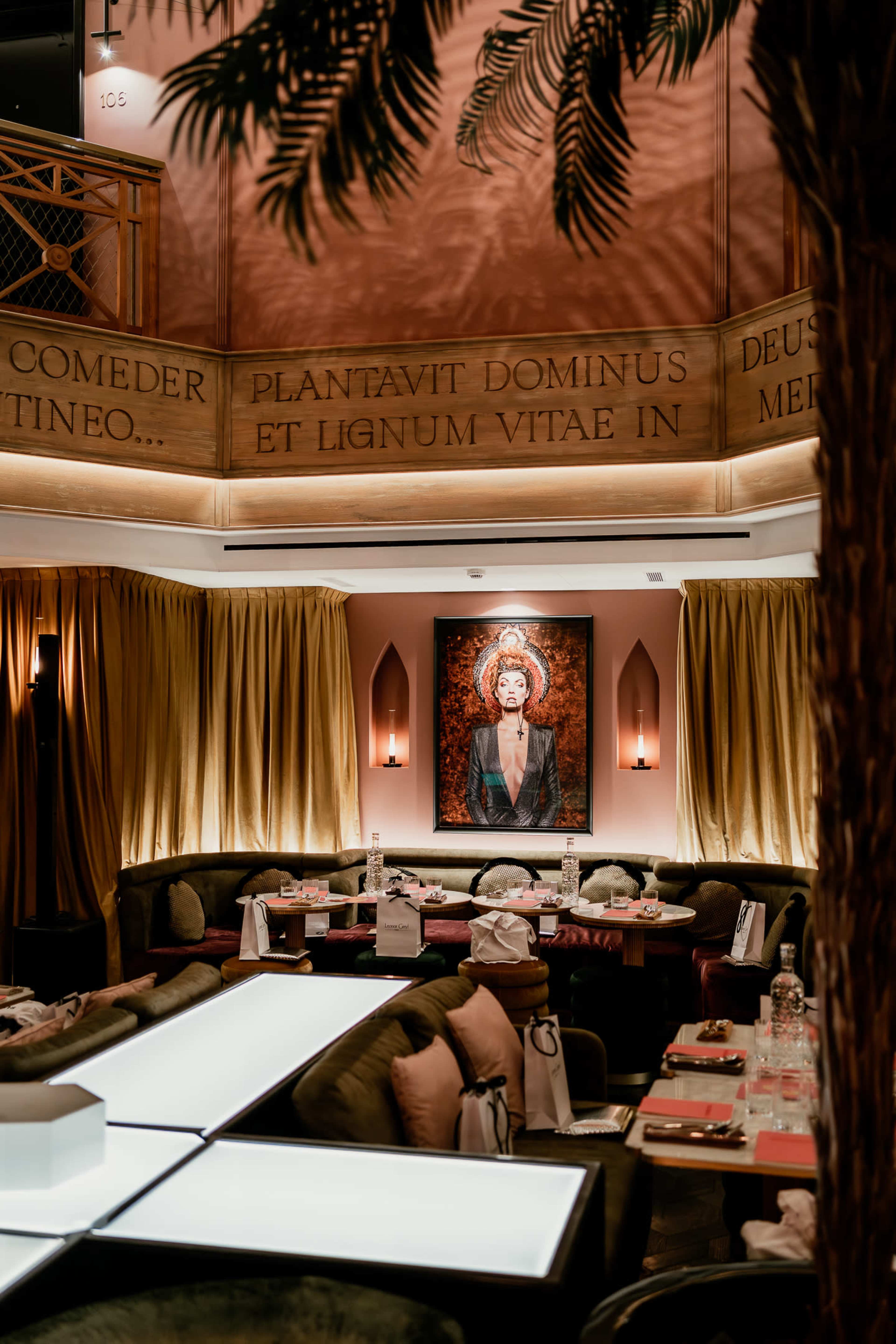 The image shows an elegant restaurant interior with plush seating, decorative curtains, and a prominent piece of artwork on the wall.
