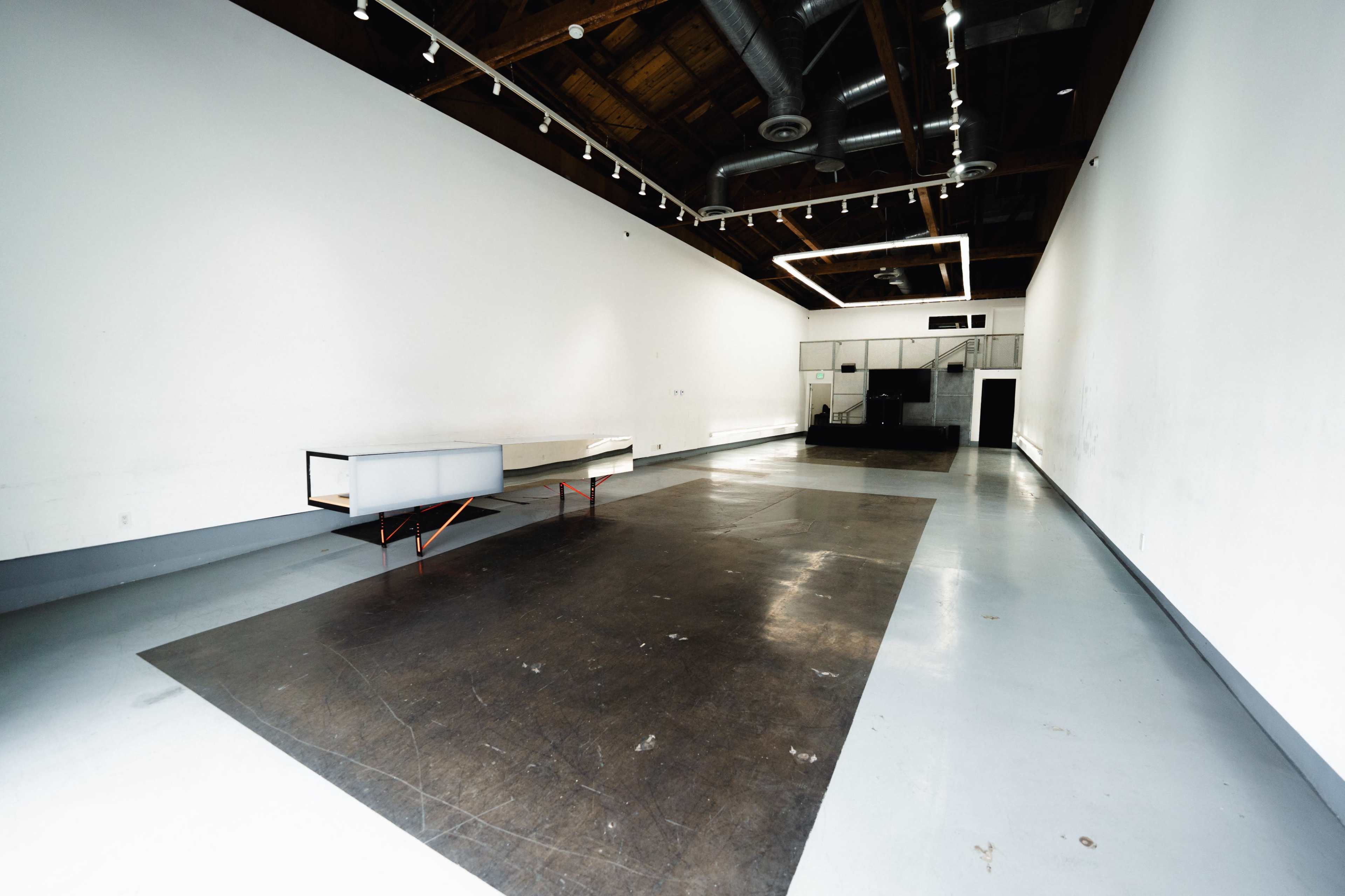 The image shows an empty, spacious interior with polished concrete floors, high ceilings, and minimal furnishings.