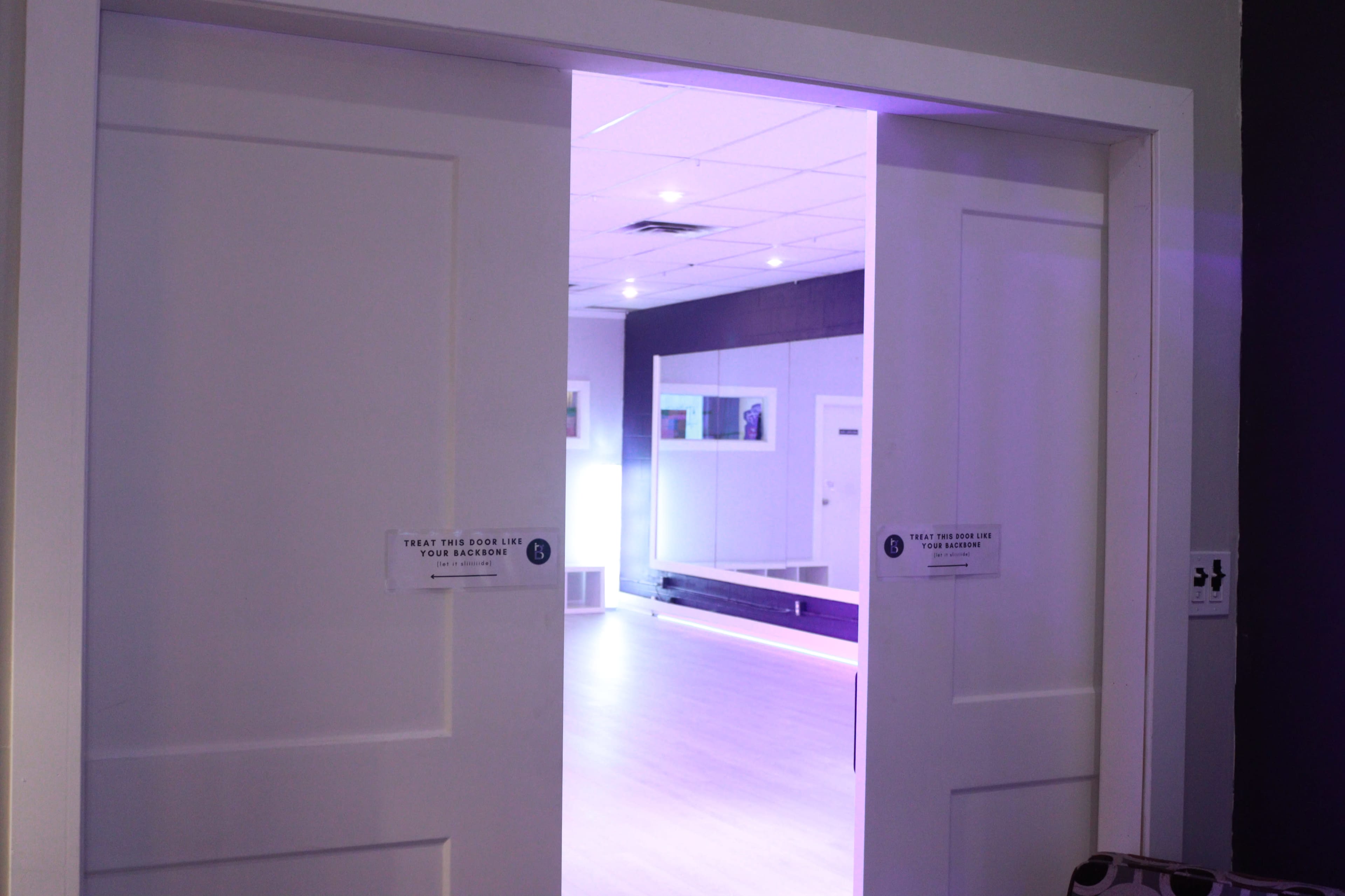 An open door leading into a brightly lit room with purple lighting and a mirrored wall.