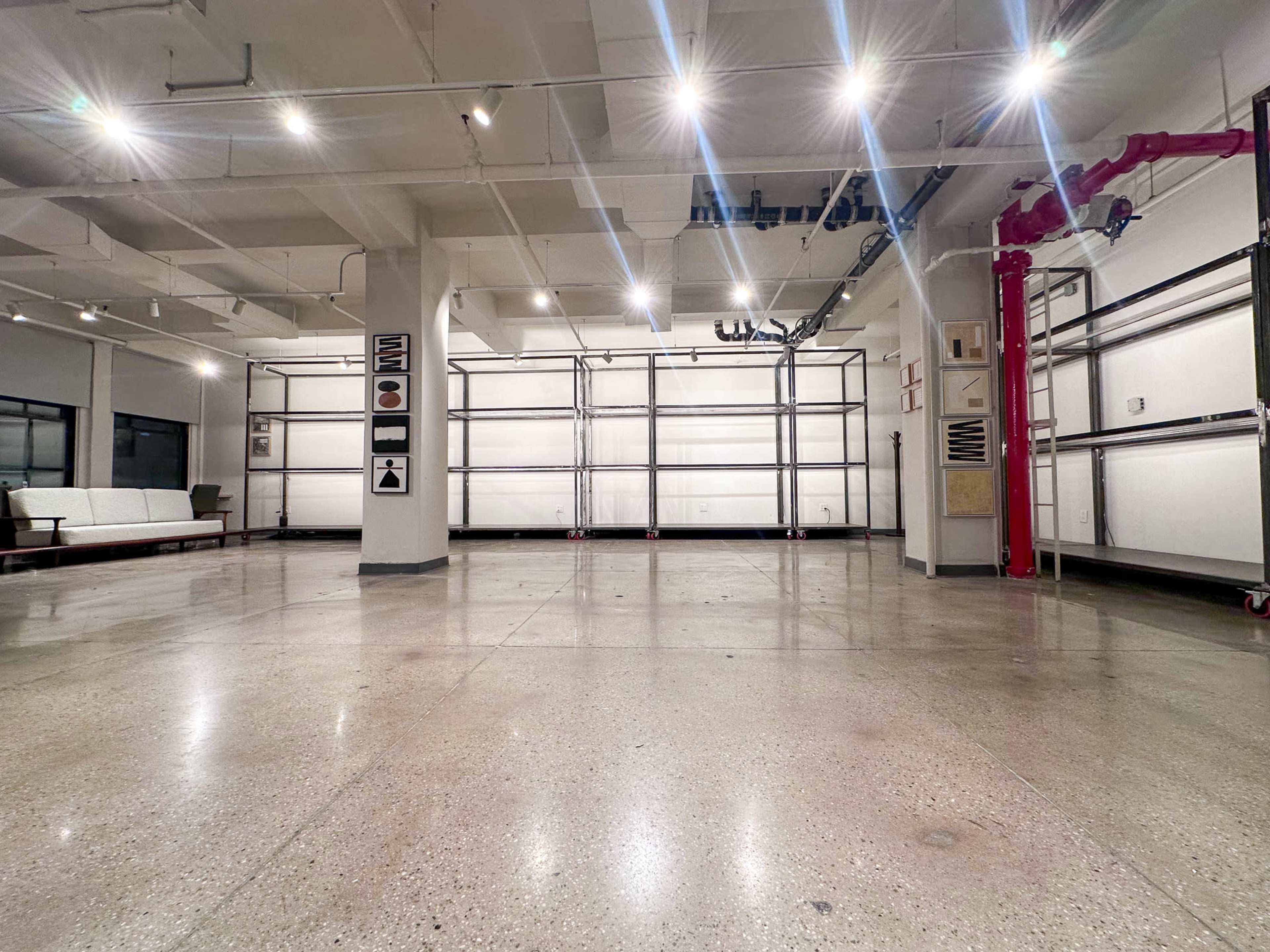 The image shows an empty industrial space with polished concrete floors, overhead lighting, and large, retractable garage doors on one side.