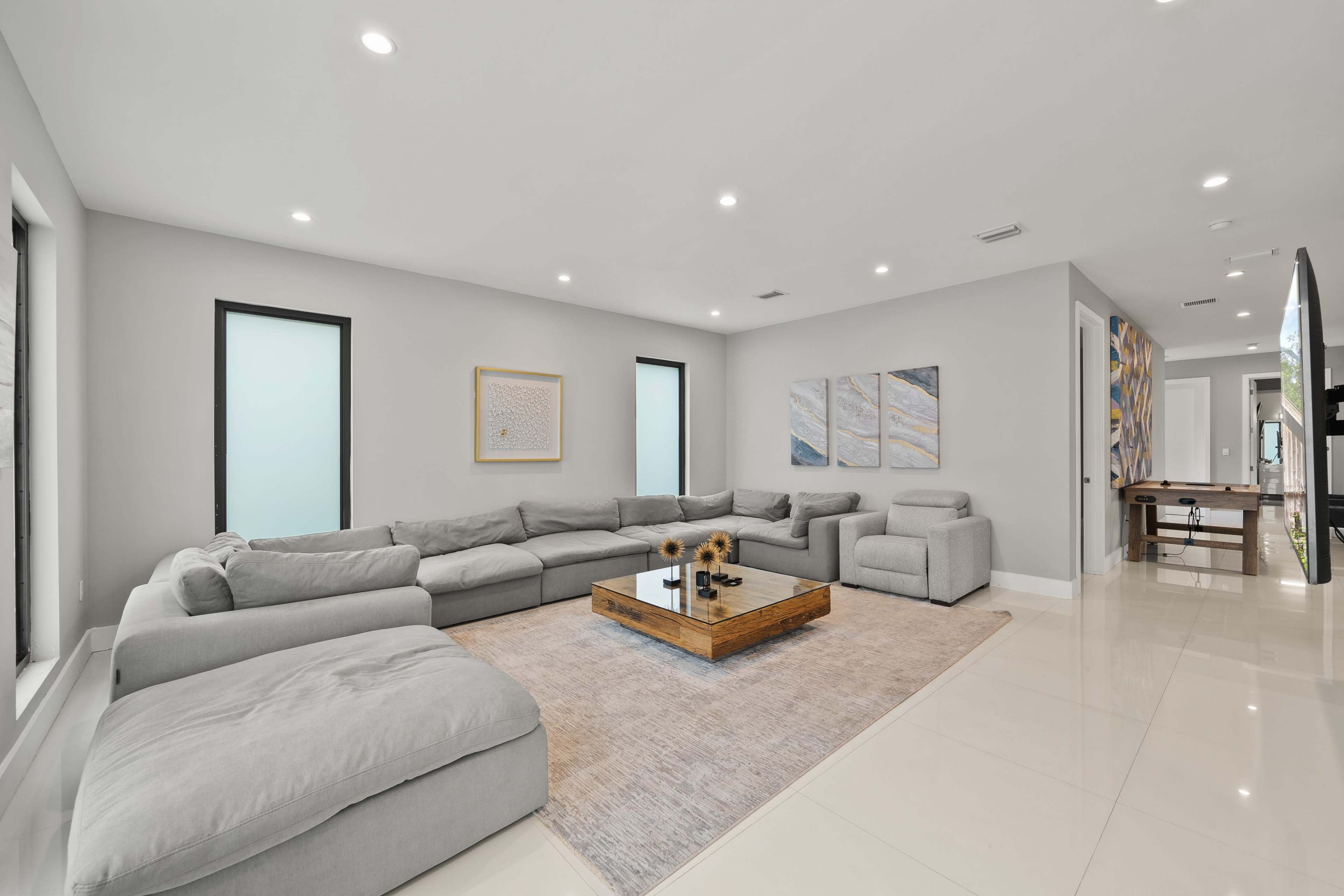 A spacious living room features a large gray sectional sofa, a coffee table on a light rug, and modern artwork on the walls.