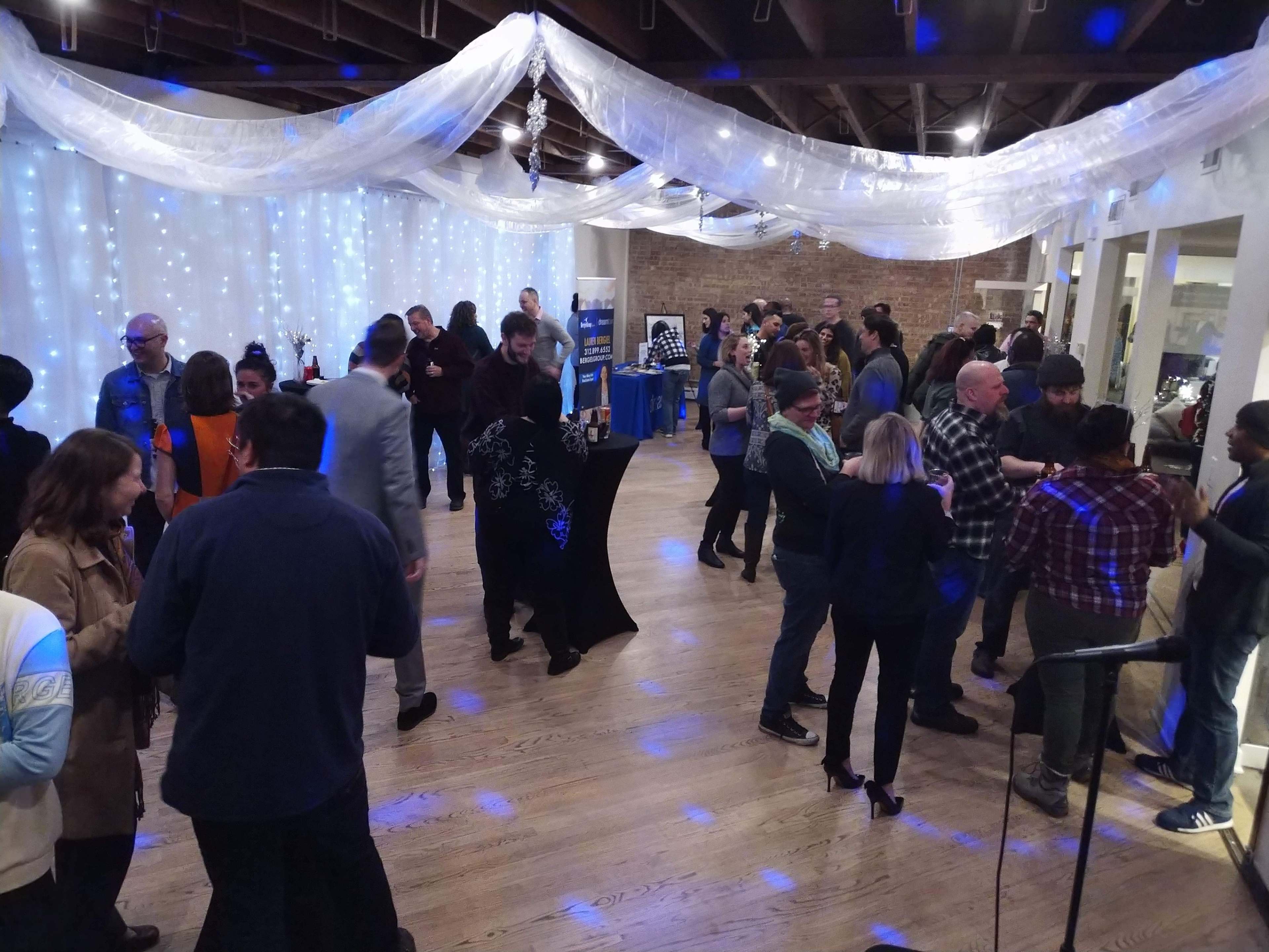 A crowded event space features people mingling under draped fabric and soft lighting.