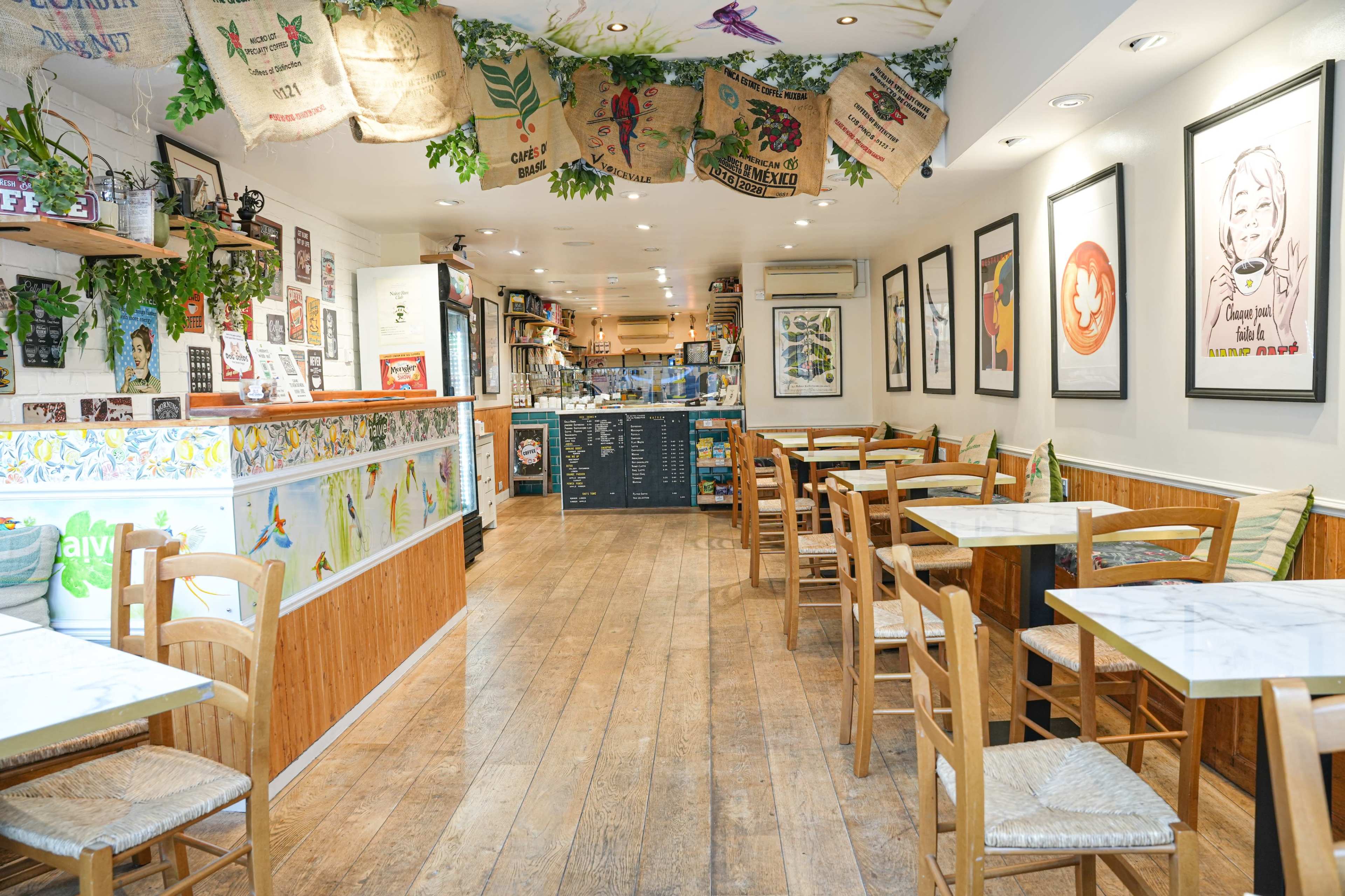 A cozy café interior with wooden tables and chairs, colorful wall art, and a counter in the background.