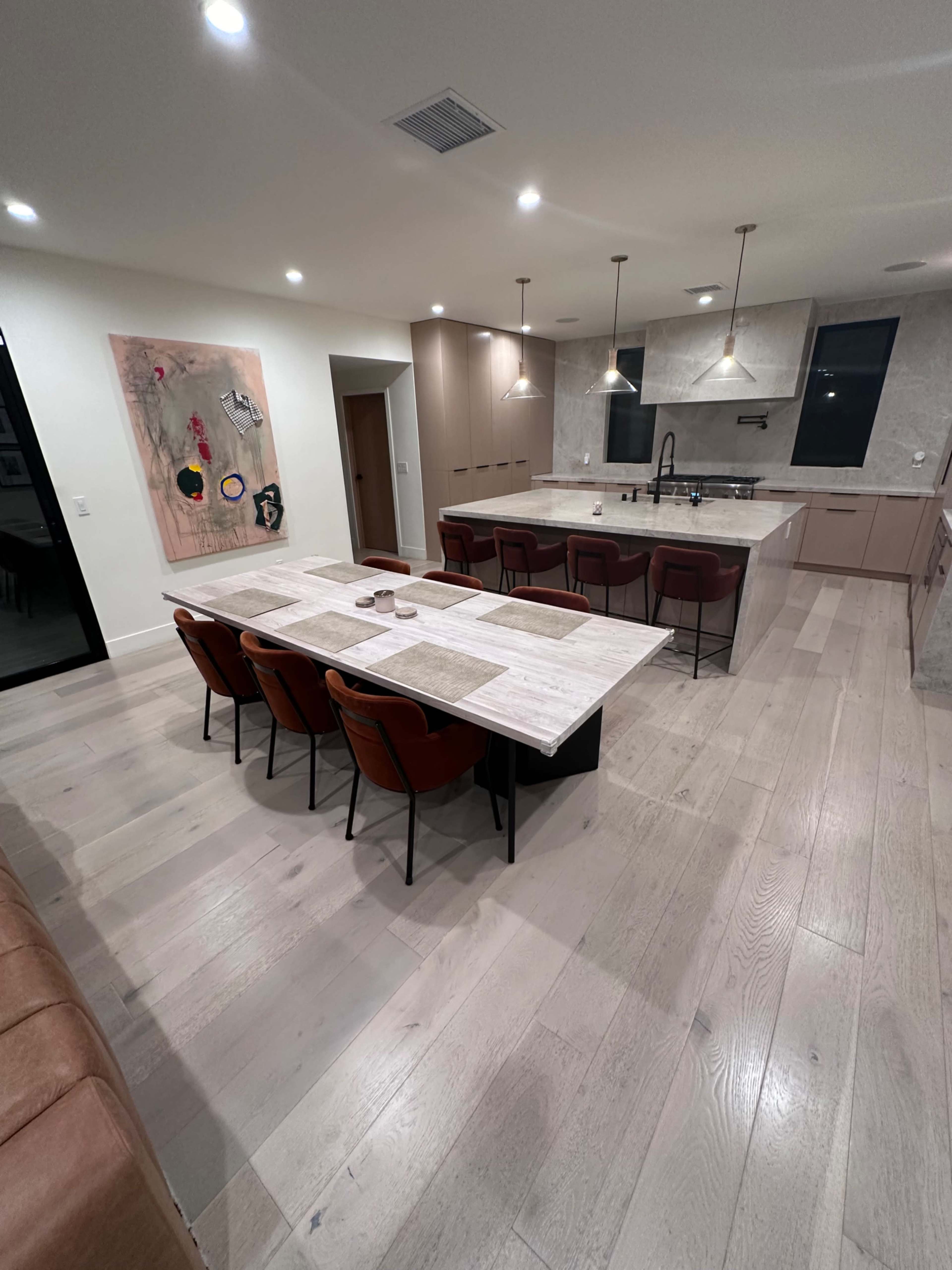 The image shows a modern kitchen and dining area featuring a large table with six chairs, a central island, and stylish cabinetry.