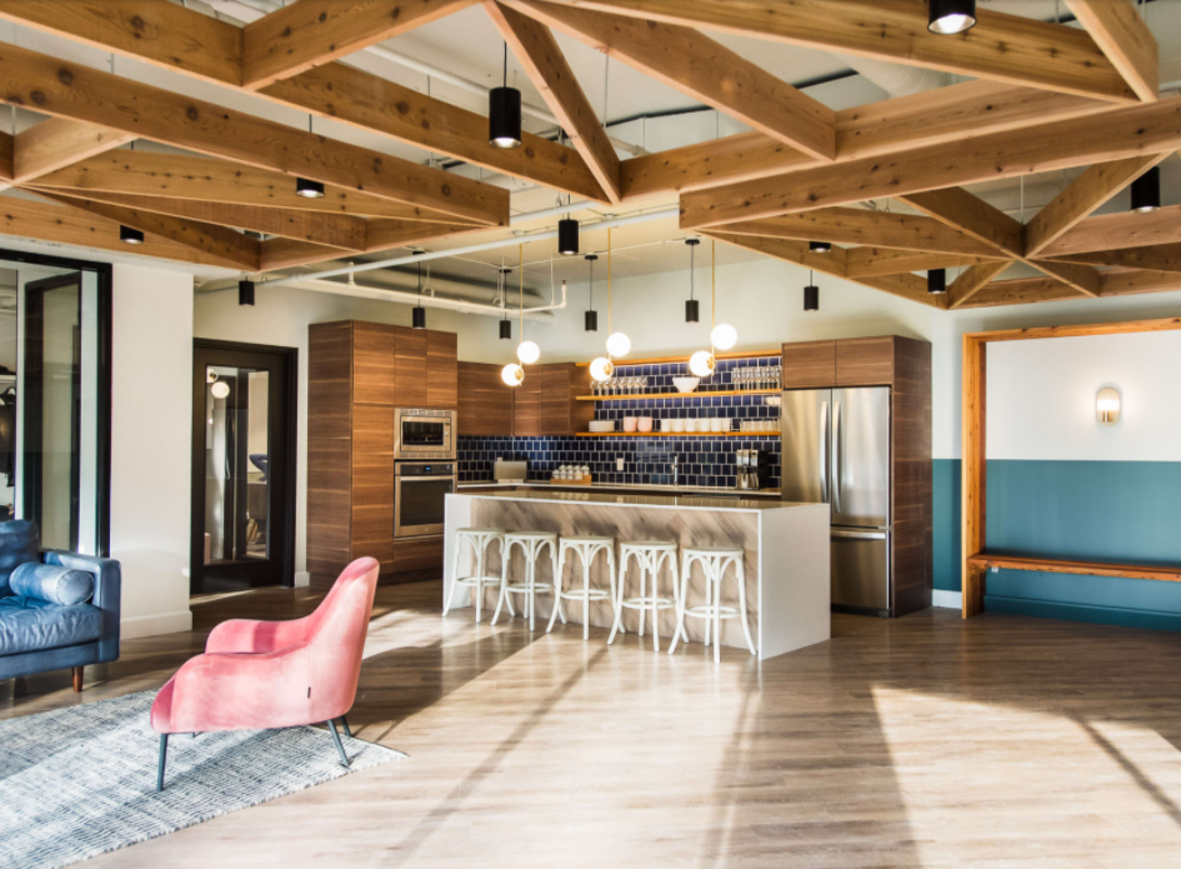 A modern kitchen with wooden beams, a central island with bar stools, and stainless steel appliances.