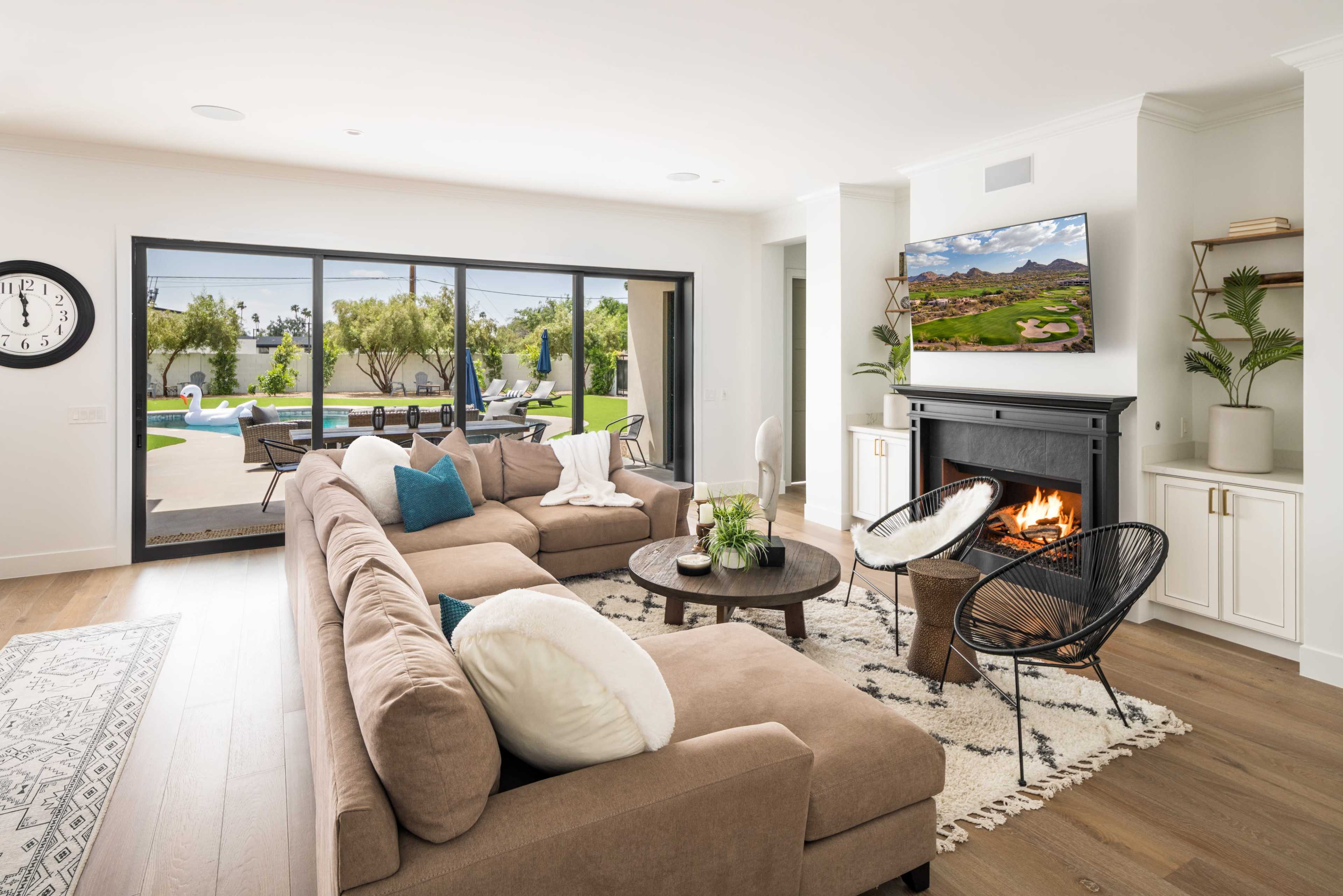 A modern living room features a large sectional sofa, a round coffee table, and a fireplace, with glass doors opening to an outdoor space with a pool.