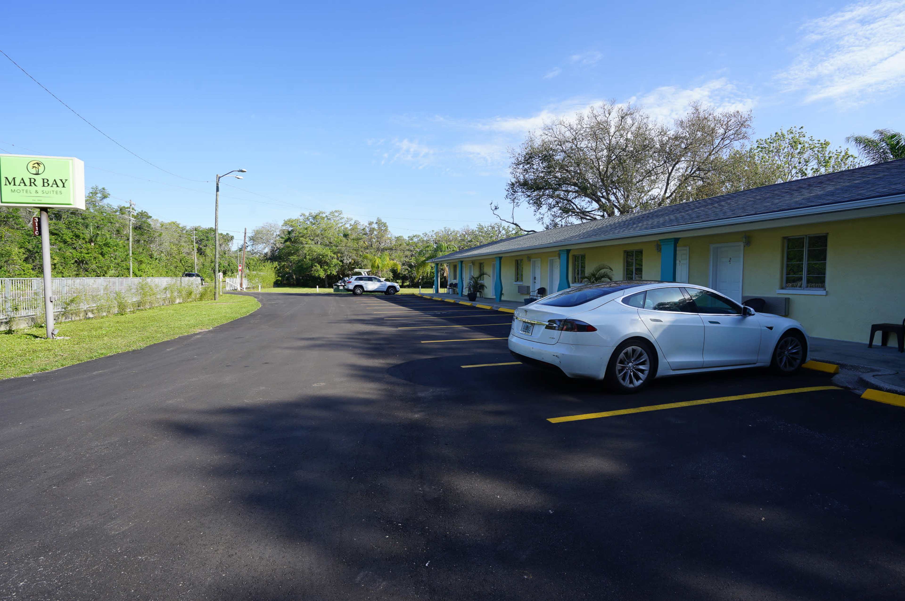 A parking area beside a motel, with two cars parked in front of the building under a clear sky.