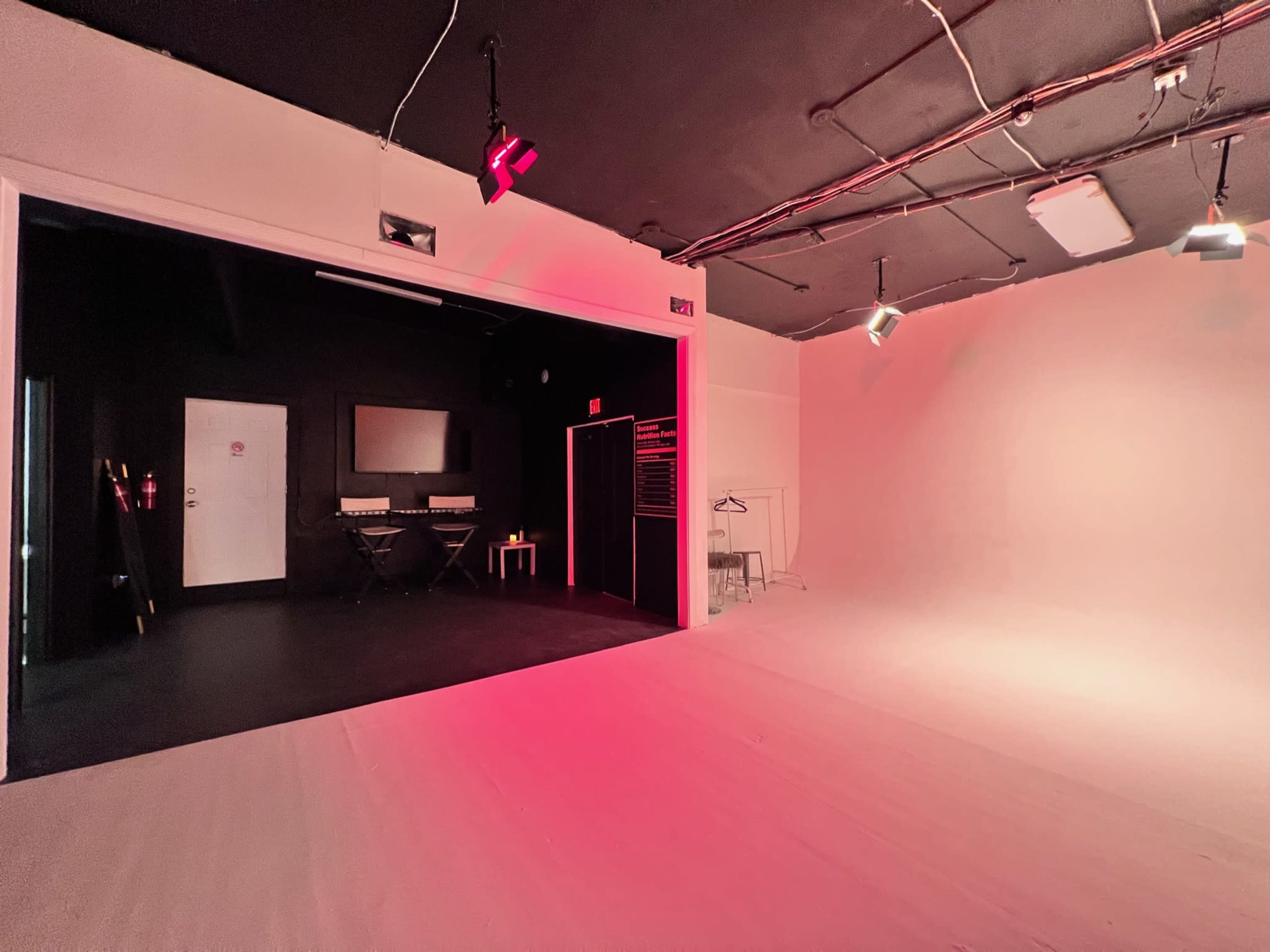 A well-lit studio space with a black section featuring a monitor and keyboard, adjacent to a light-colored, empty area with smooth flooring.