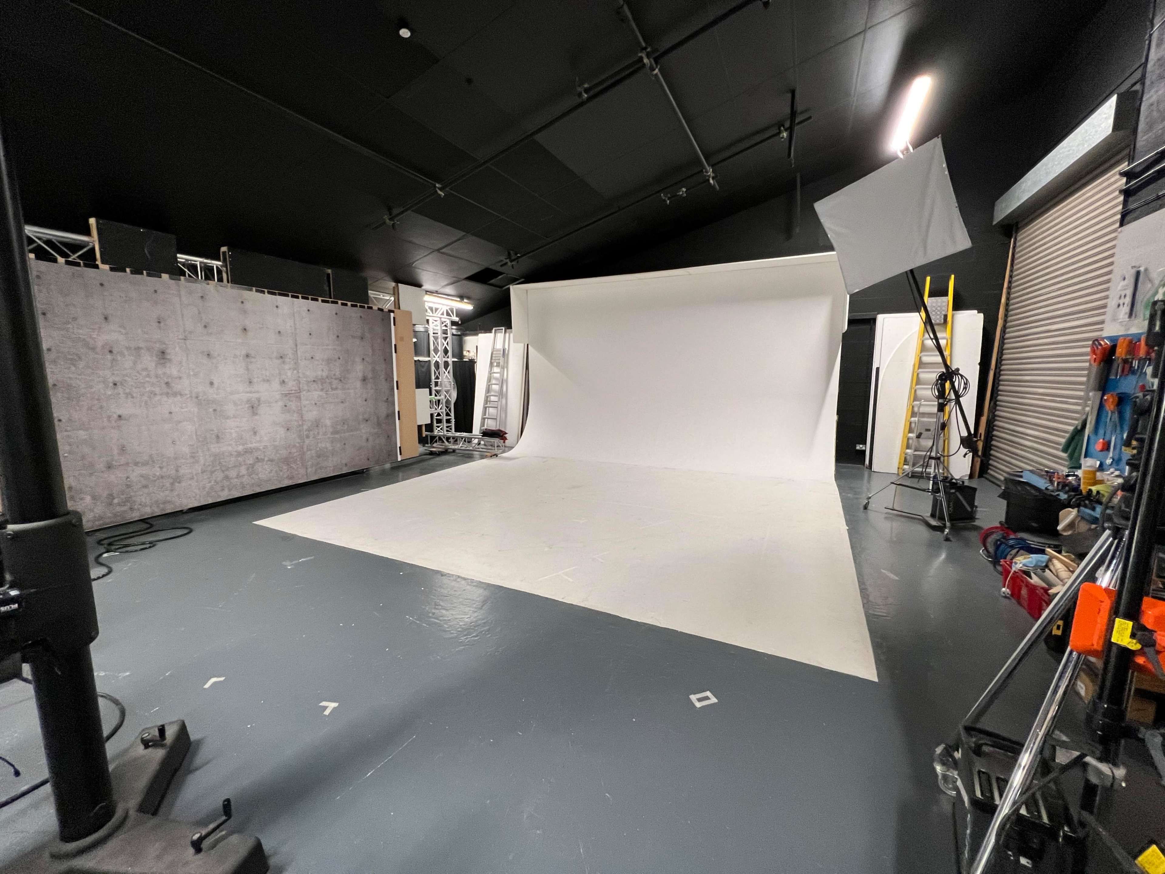 A photography studio featuring a large white backdrop, various equipment, and a ladder against the wall.