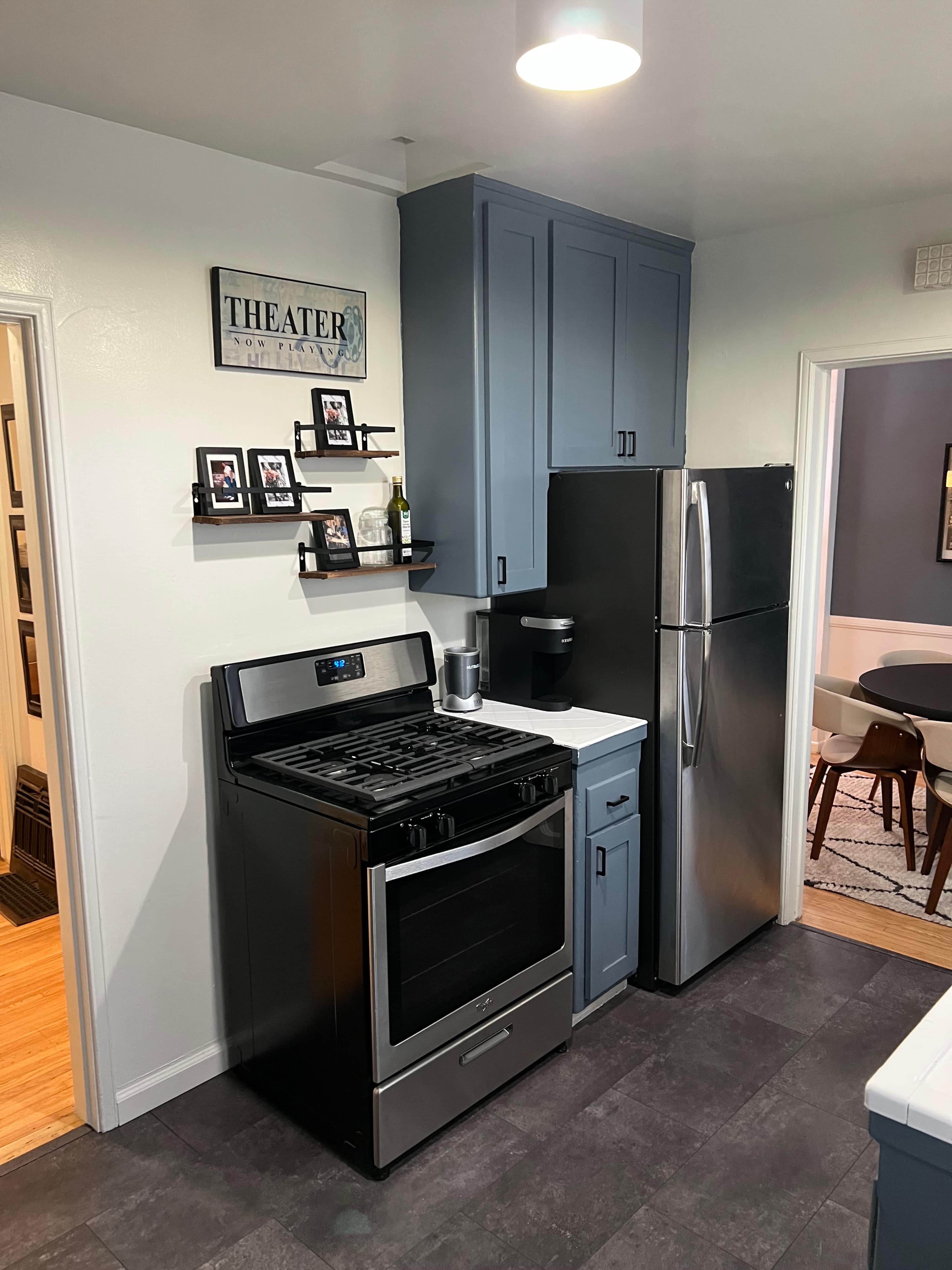 A modern kitchen features a gray stove and refrigerator, with navy blue cabinets and framed pictures on the wall.