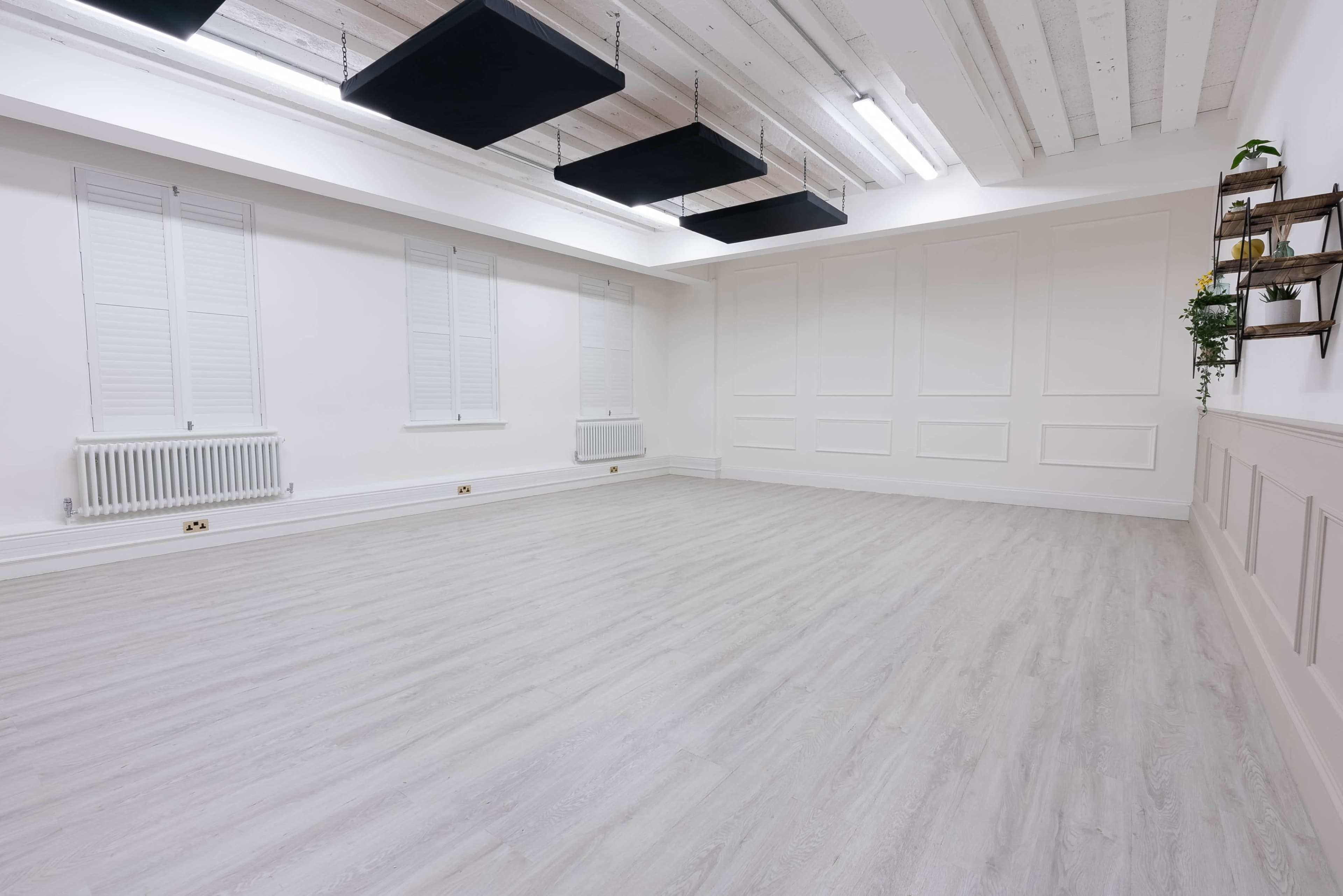 A spacious, empty room with white walls, light gray flooring, and a few windows.
