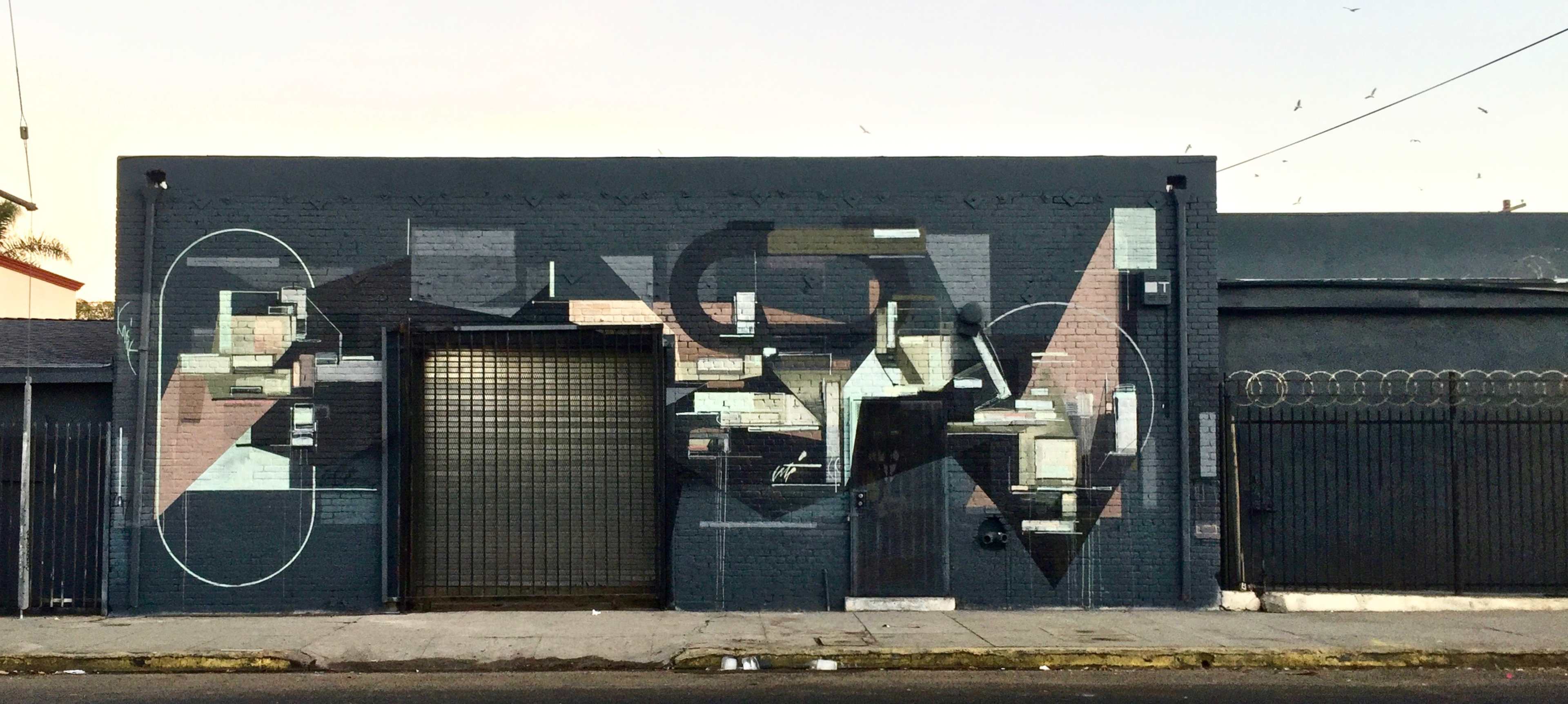 The image shows a mural on the exterior wall of a building, featuring geometric shapes and abstract designs in various colors.