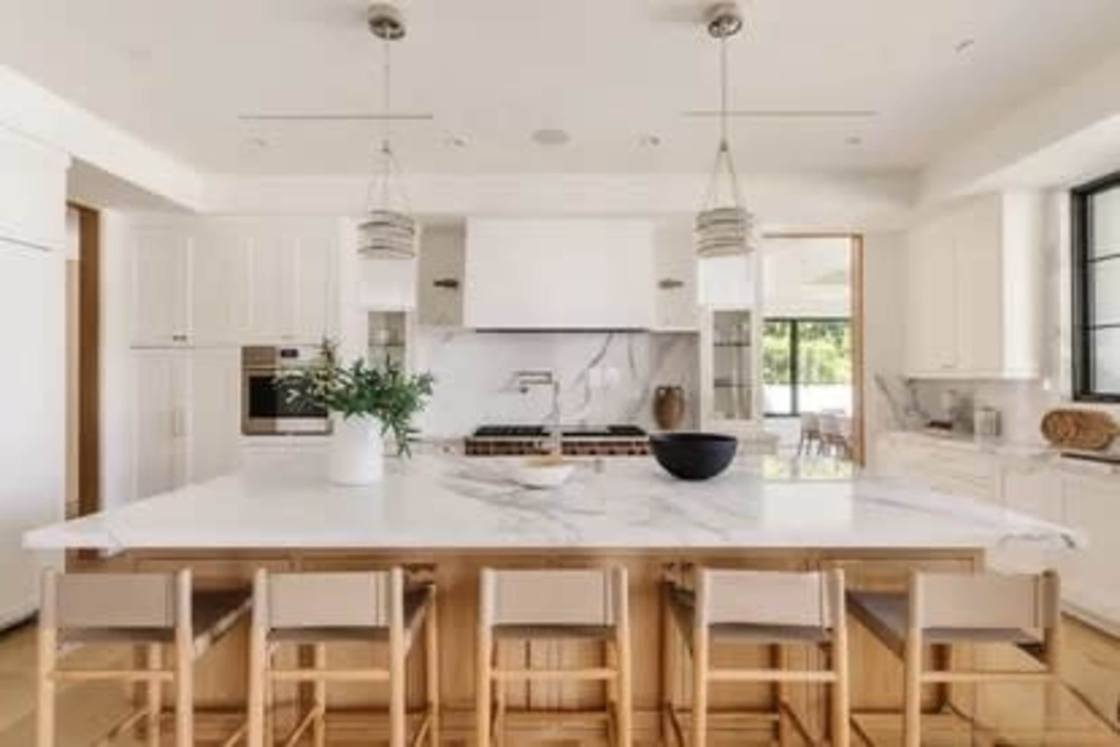 A modern kitchen features a large marble island with seating, white cabinetry, and a minimalist design.