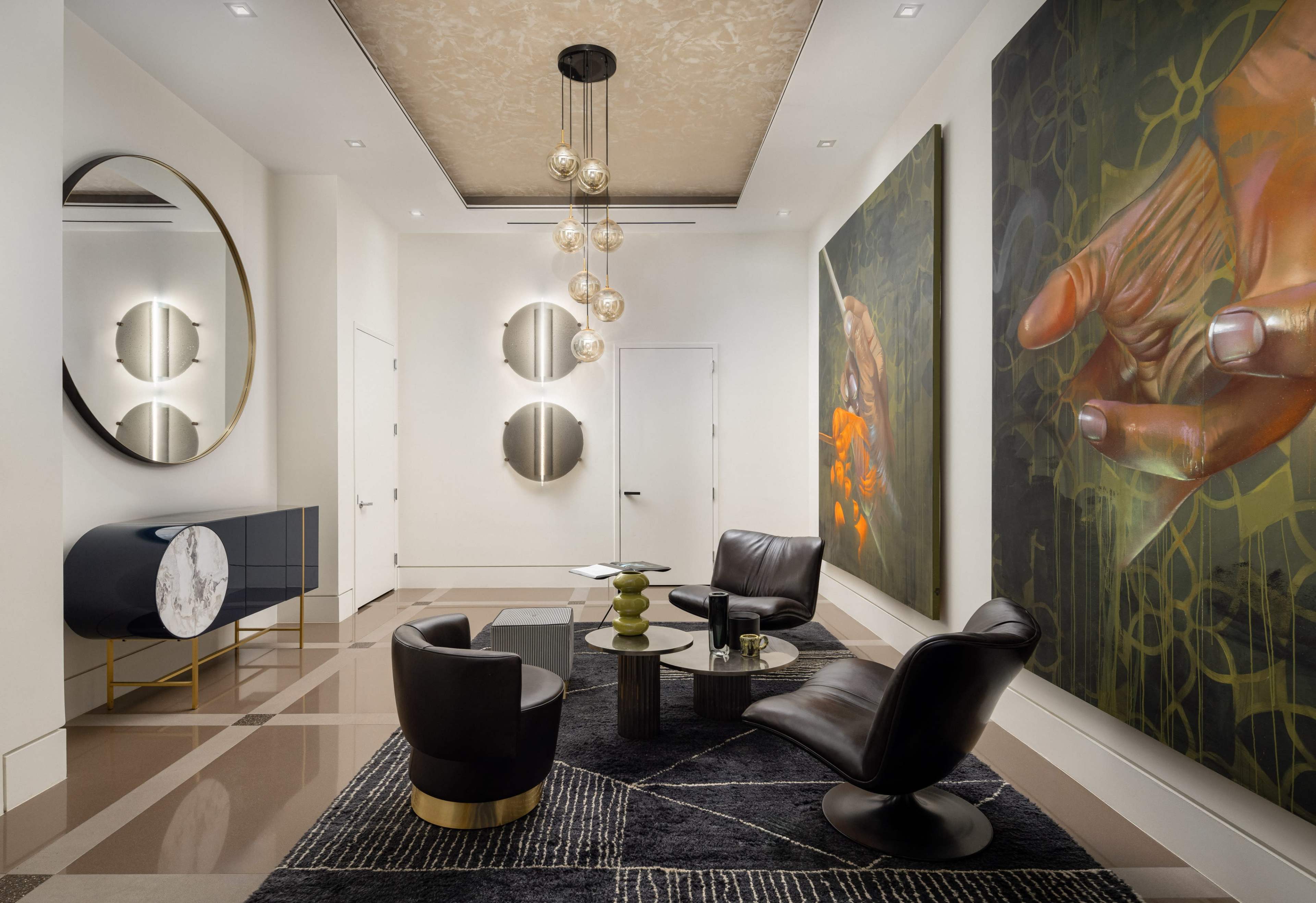 The image shows a modern lounge area with black leather chairs, a round coffee table, and large abstract paintings on the walls.