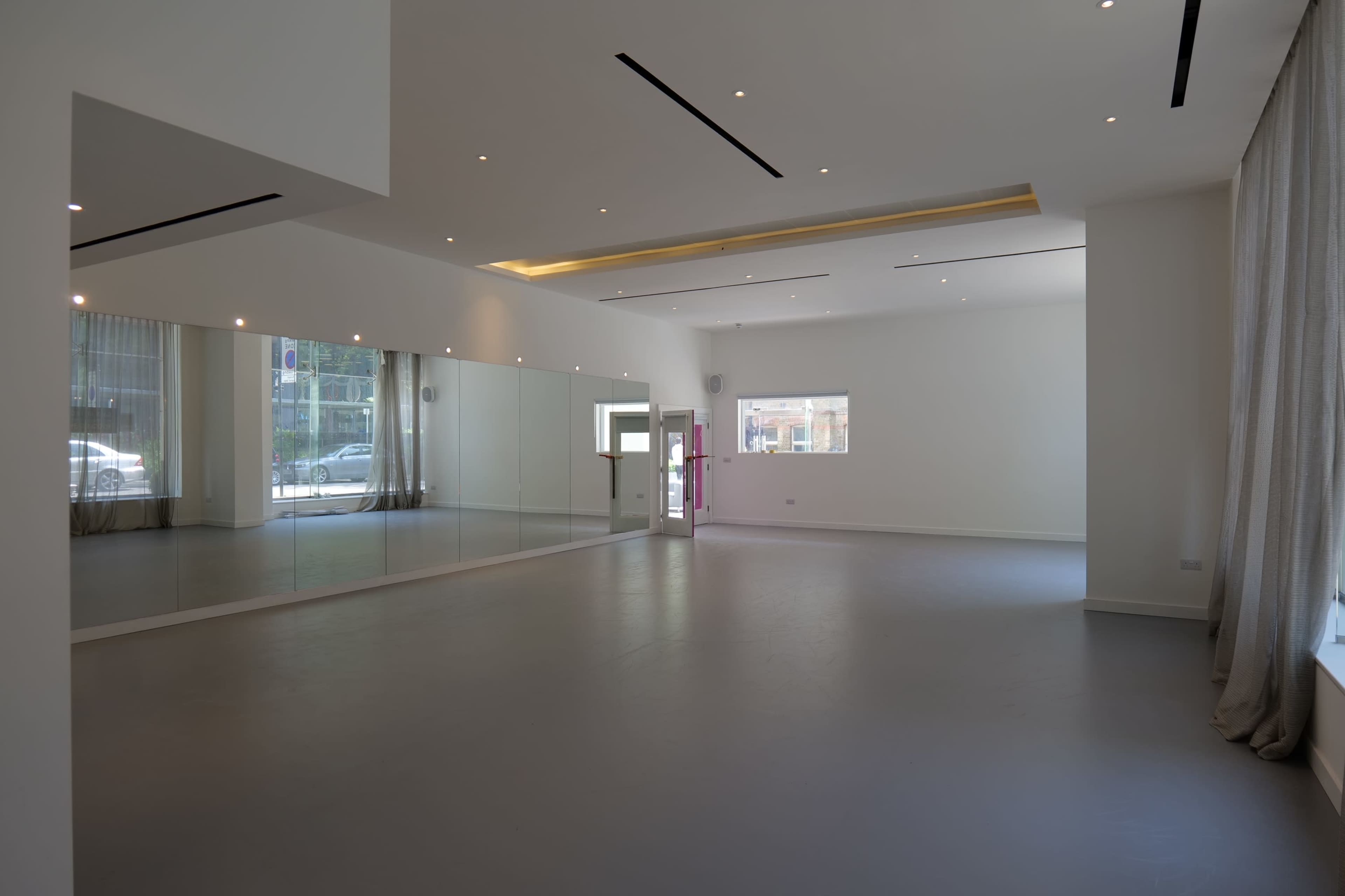 An empty studio space with a large mirror on one wall and natural light coming through a window.