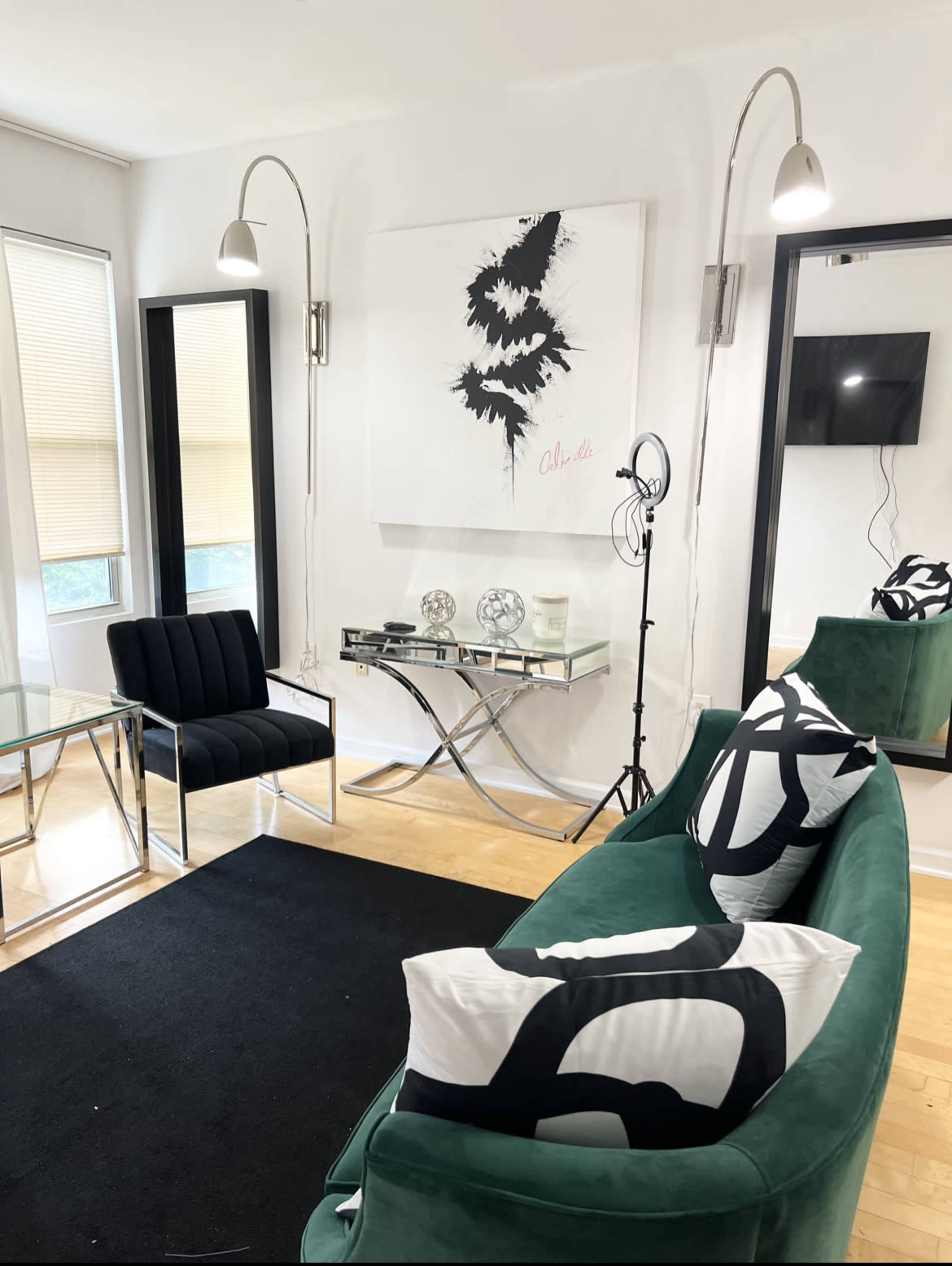 A modern living room featuring a green sofa with black and white patterned pillows, a glass coffee table, and contemporary decor elements, including an abstract artwork on the wall and a television.