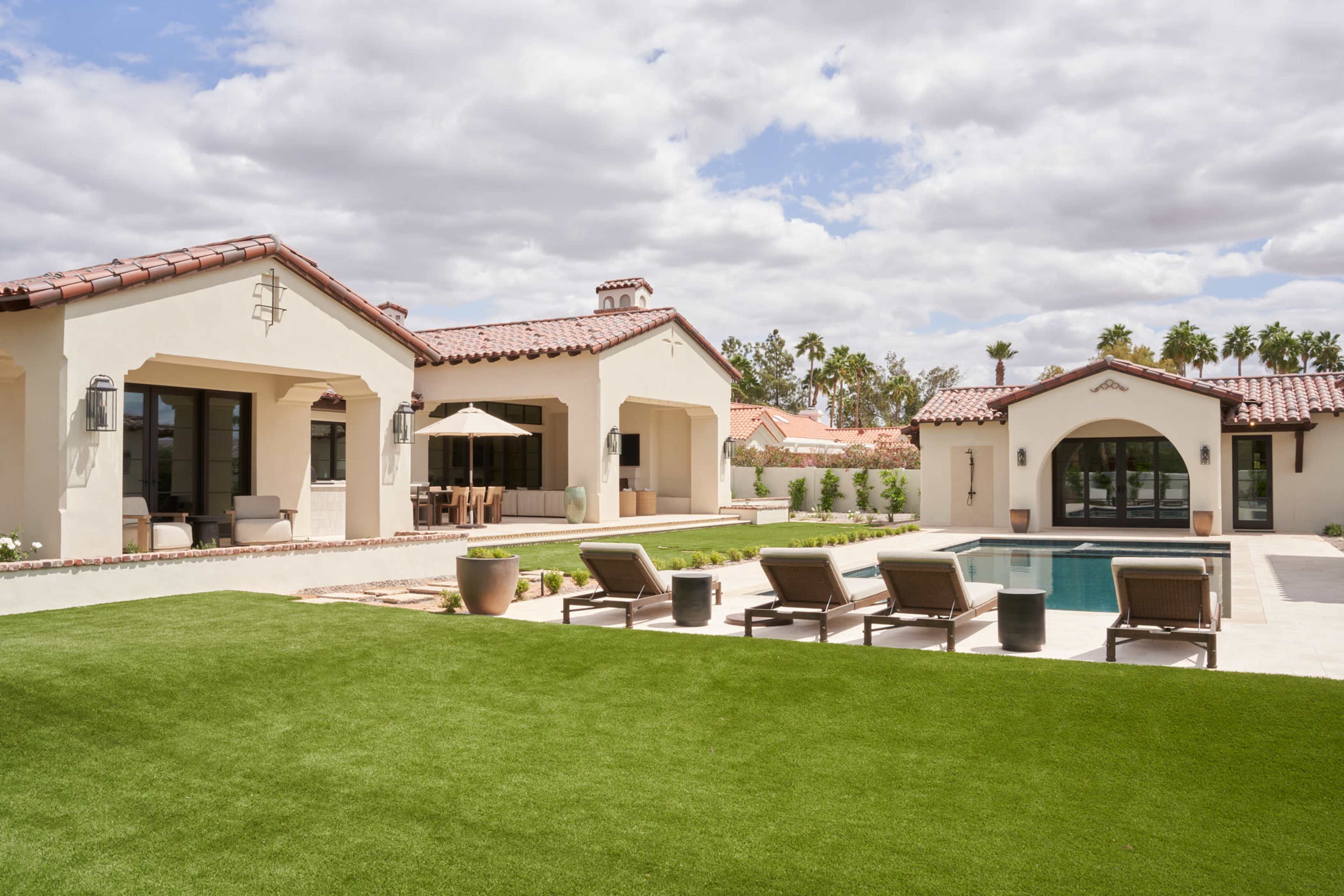 The image shows a modern-style home with two structures surrounding a swimming pool, featuring a well-manicured lawn and patio furniture.