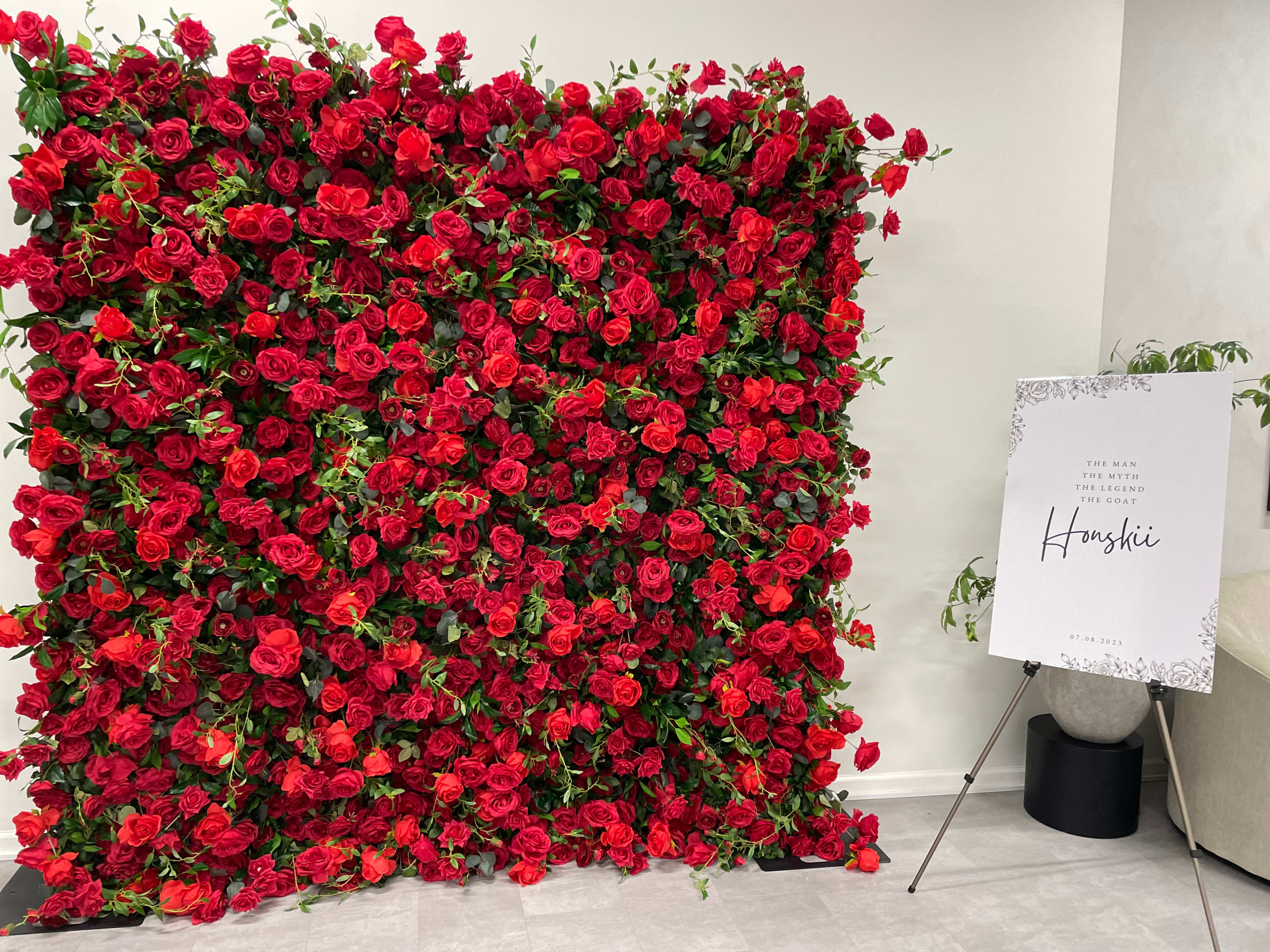 A wall covered in red roses stands next to a sign on an easel that displays the word "Hangshi."