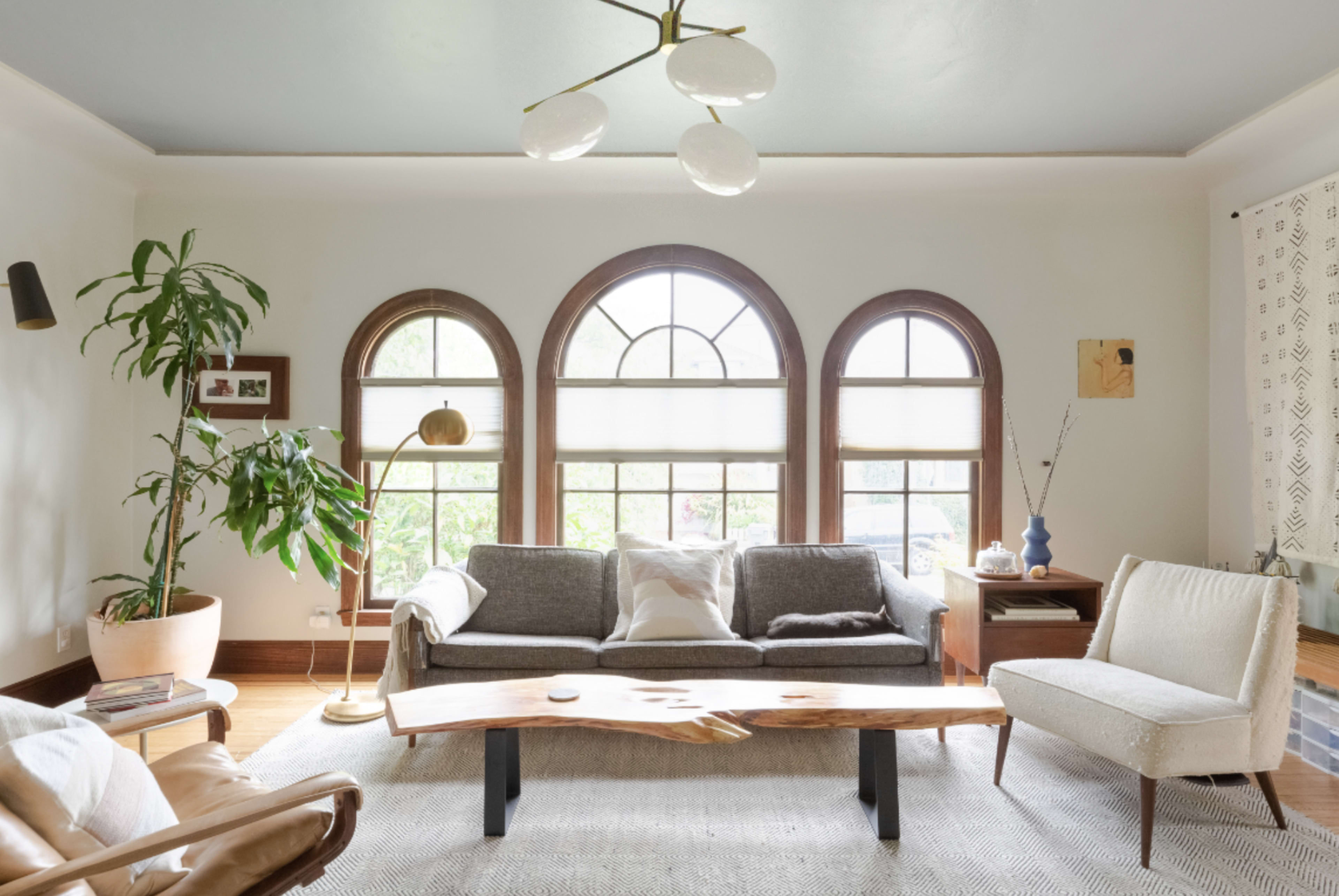 The living room features a light-colored sofa and an armchair arranged around a wooden coffee table, with large arched windows allowing natural light to fill the space.