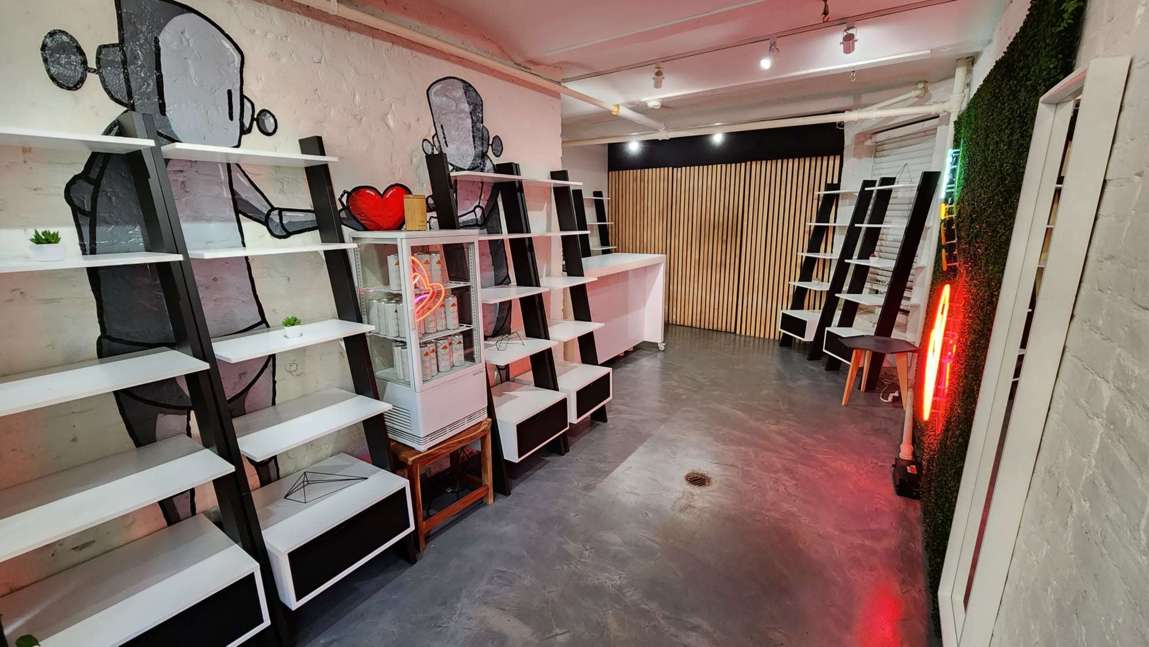 A stylish, empty interior space featuring white shelves along the walls, a glass display case, and a decorative neon light.