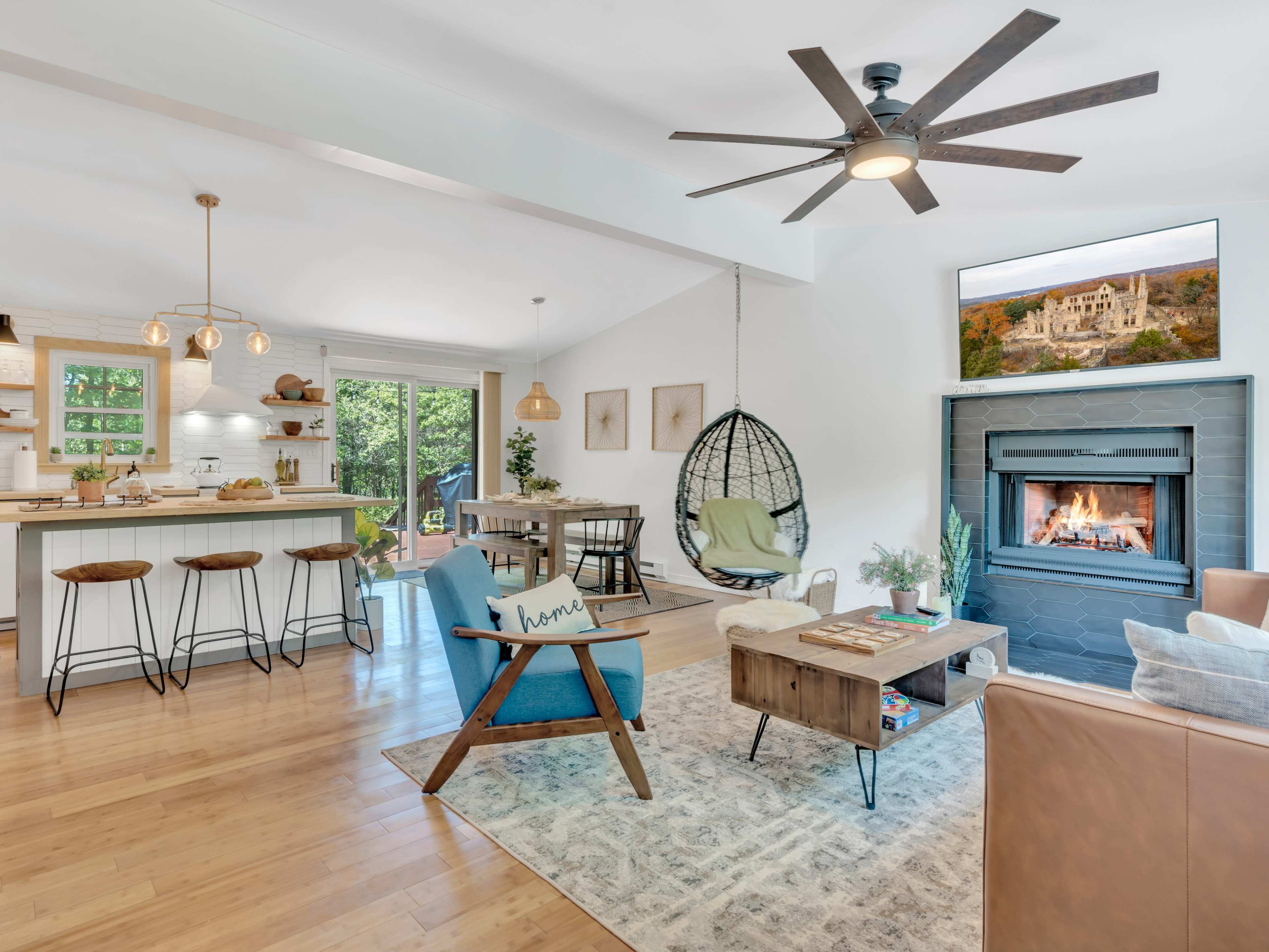 The image shows a modern open-concept living space featuring a cozy seating area, a dining table, and a kitchen island, all illuminated by natural light.