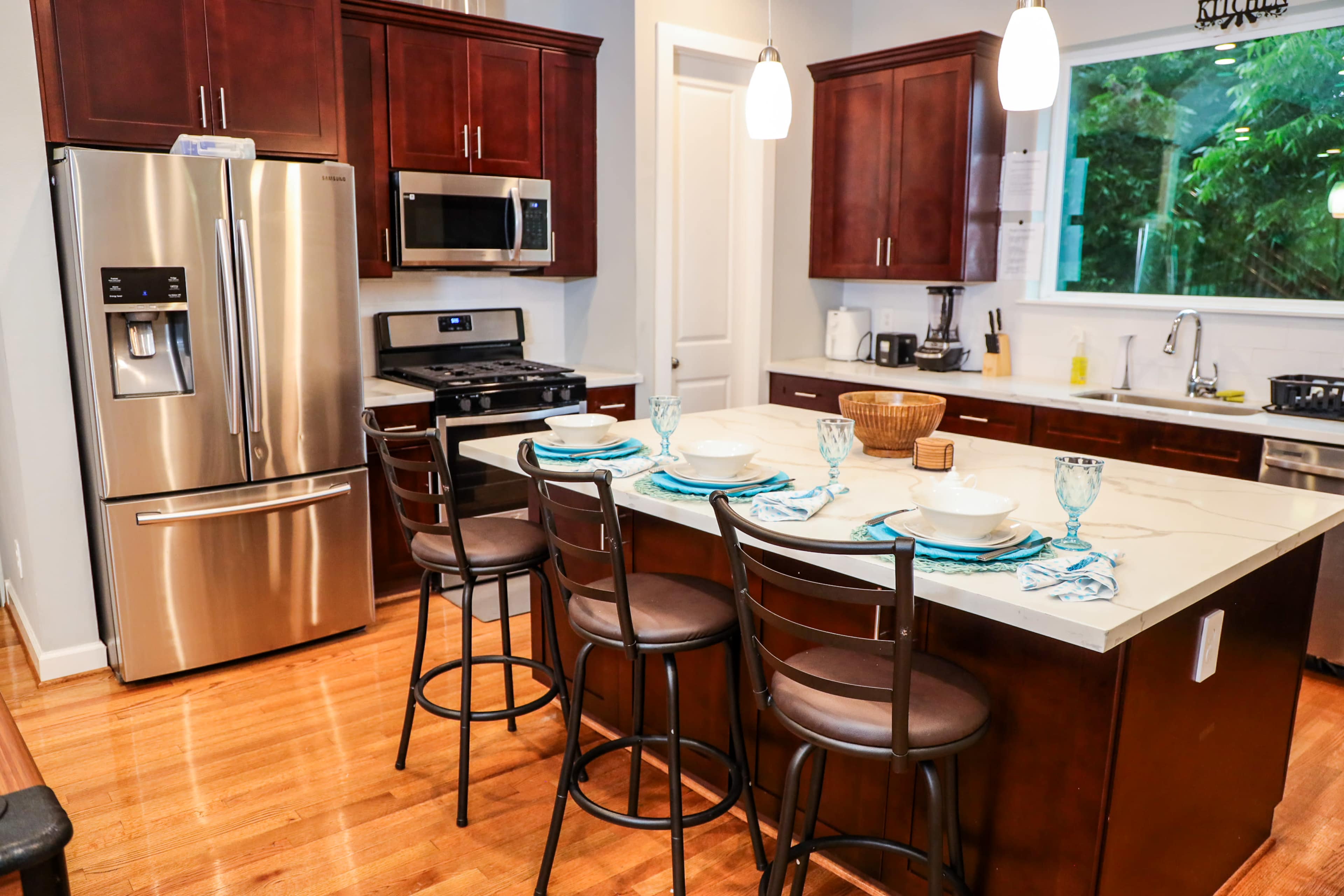A modern kitchen features dark wood cabinetry, stainless steel appliances, and a large island with seating for four.