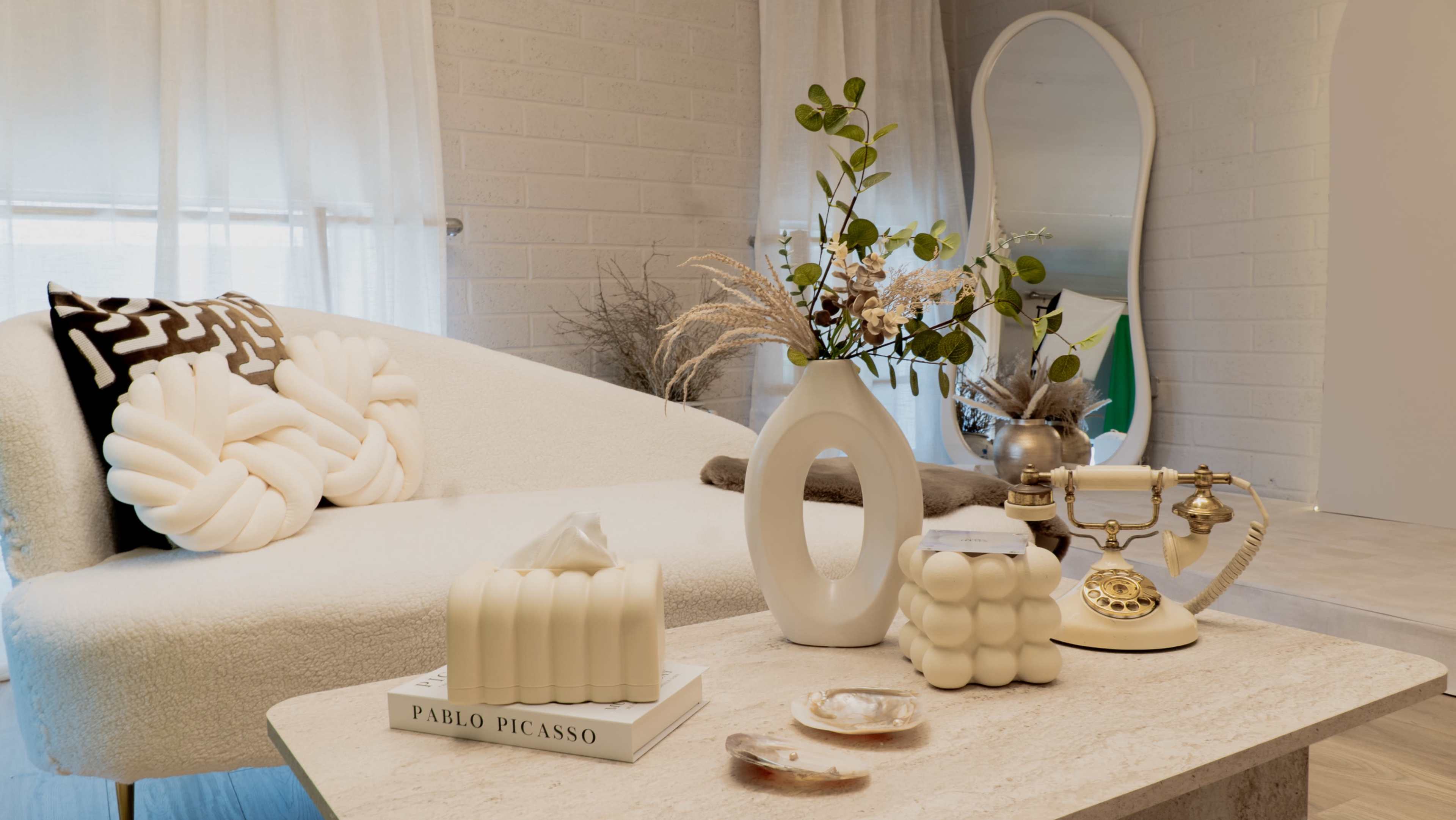 The scene features a modern living room with a plush sofa, a decorative vase, various artistic objects, and a vintage telephone on a coffee table.