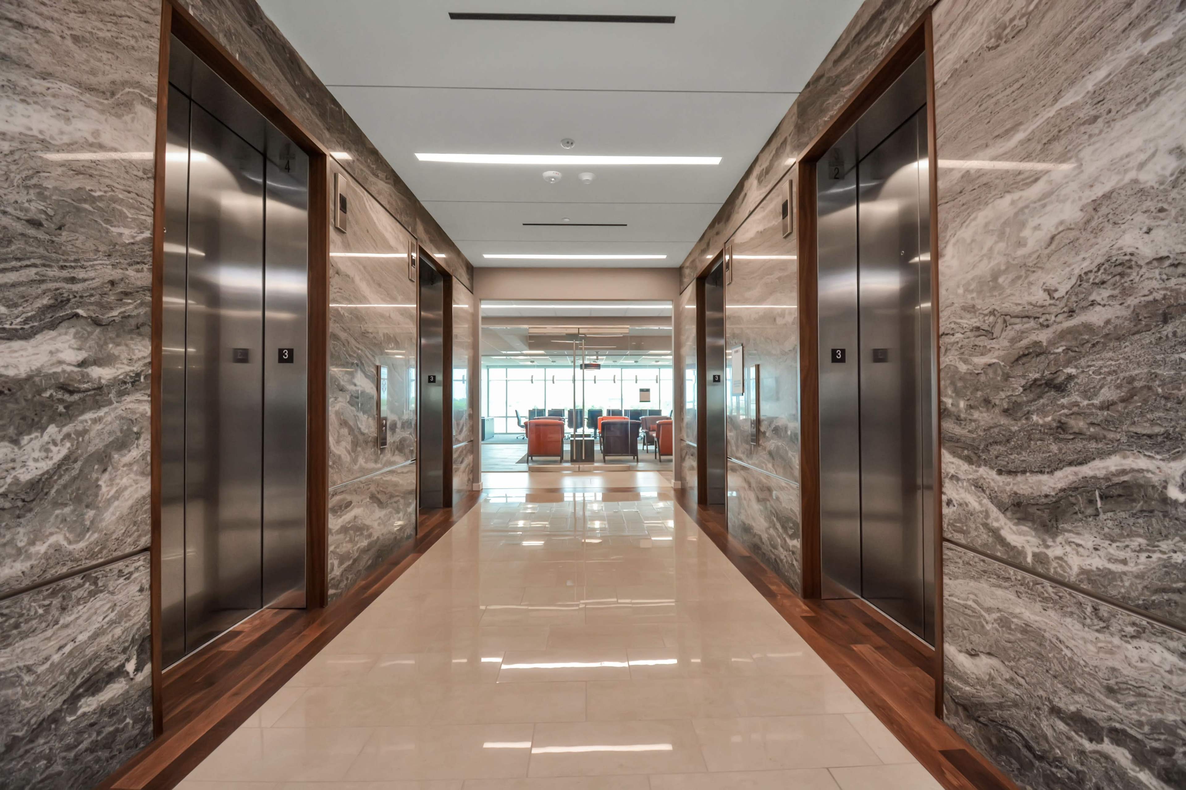 A hallway features two sets of elevator doors on either side, with a seating area visible at the end.