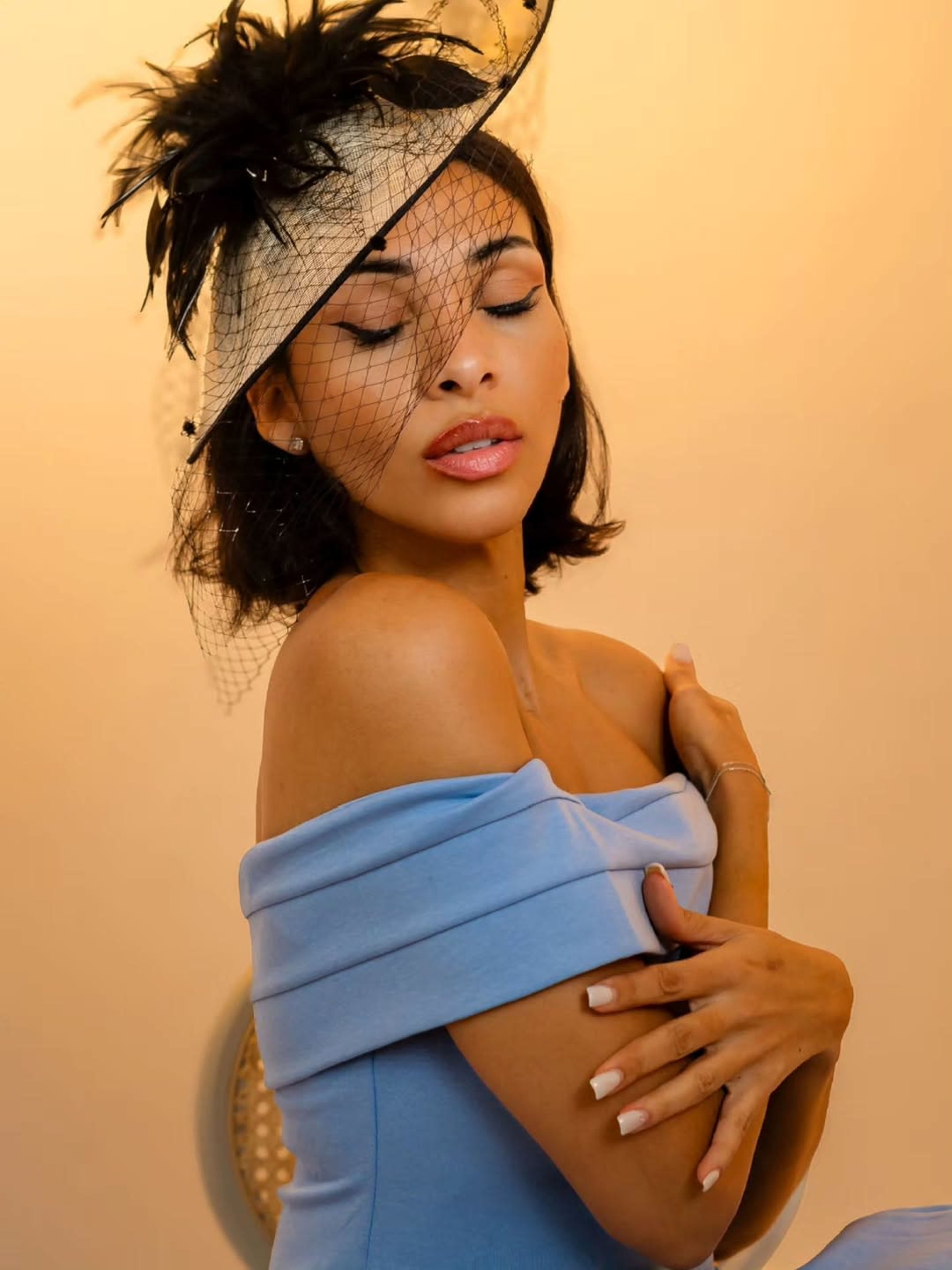 A woman in a blue off-shoulder dress poses elegantly while wearing a wide-brimmed hat.